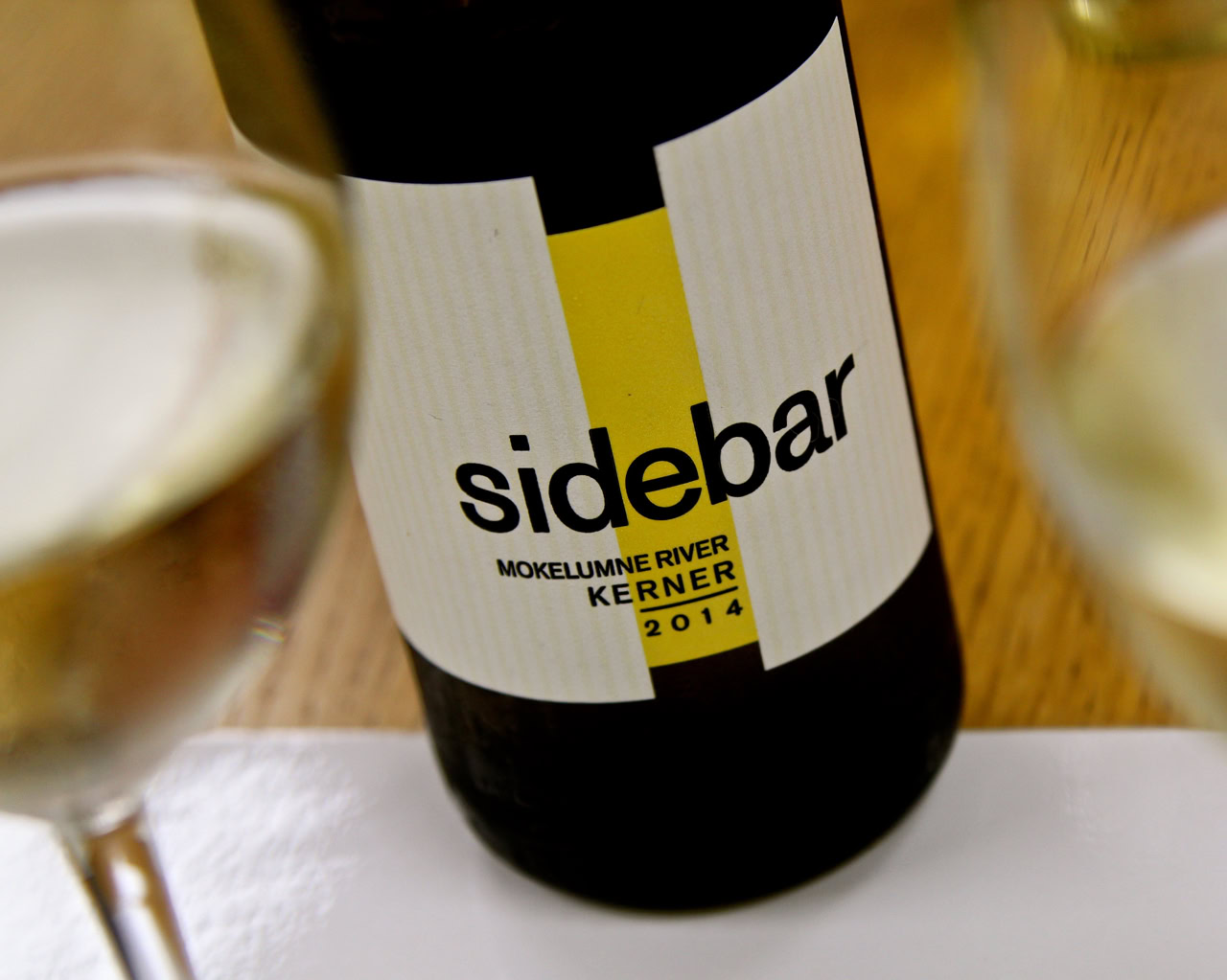 Close-up of a wine bottle labeled 'sidebar' from Mokelumne River KERNER 2014, with wine glasses in the background.