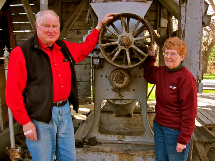 Two people standing beside a vintage wine press at Lodi Winegrape Commission.