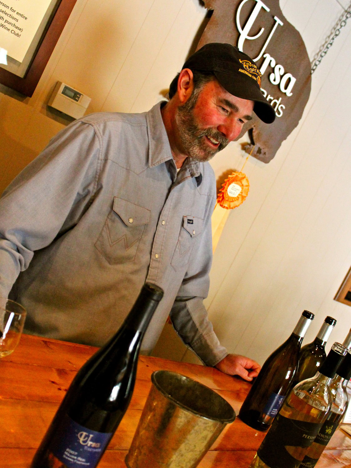 Smiling man at wine tasting event with bottles of wine on table.