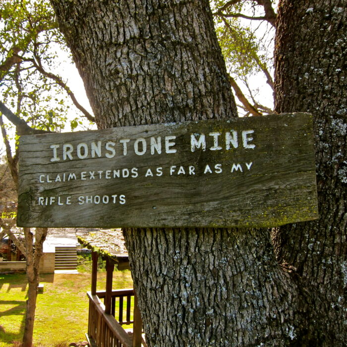 Old wooden sign on tree reading 'Ironstone Mine' with historical info.