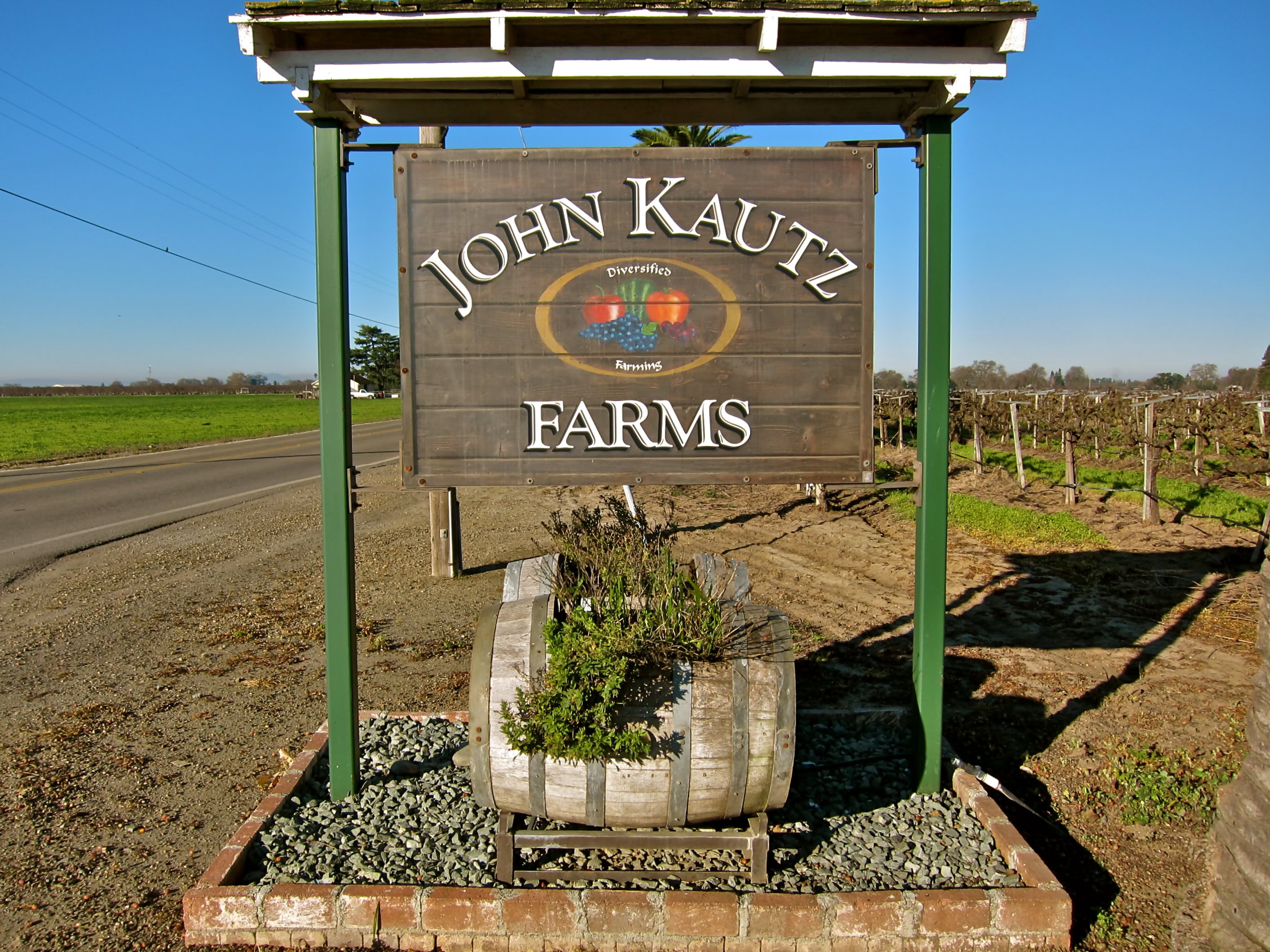 Entrance sign for John Kautz Farms, a vineyard in Lodi, California, with grapevines in the background.