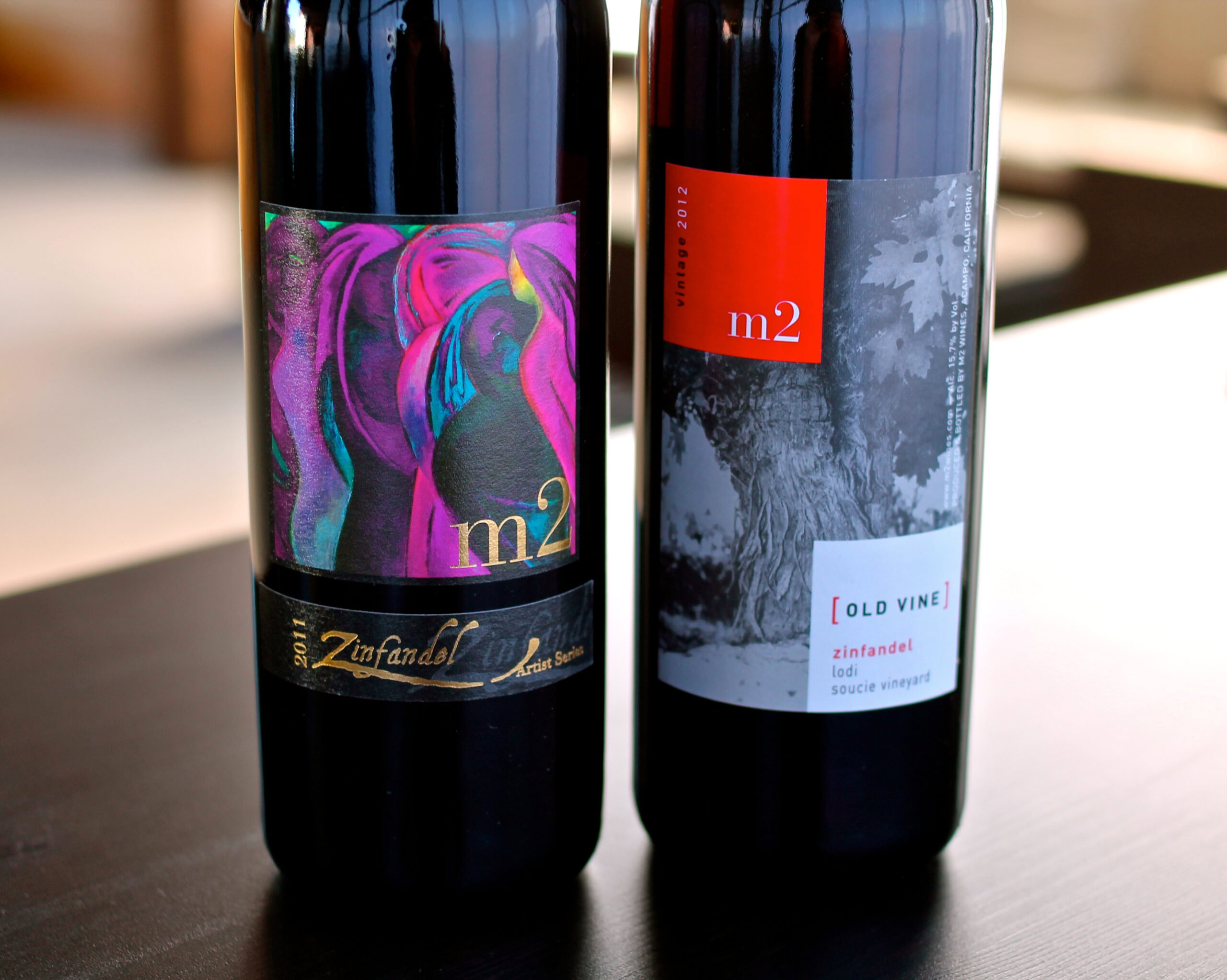 Two wine bottles from Lodi Winegrape Commission with colorful and modern labels on a dark surface.