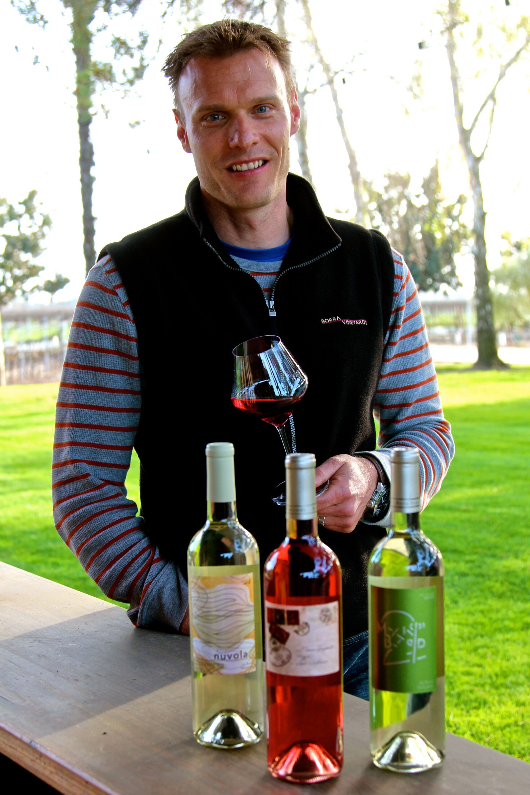Man showcasing three bottles of wine at an outdoor event for Lodi Winegrape Commission.