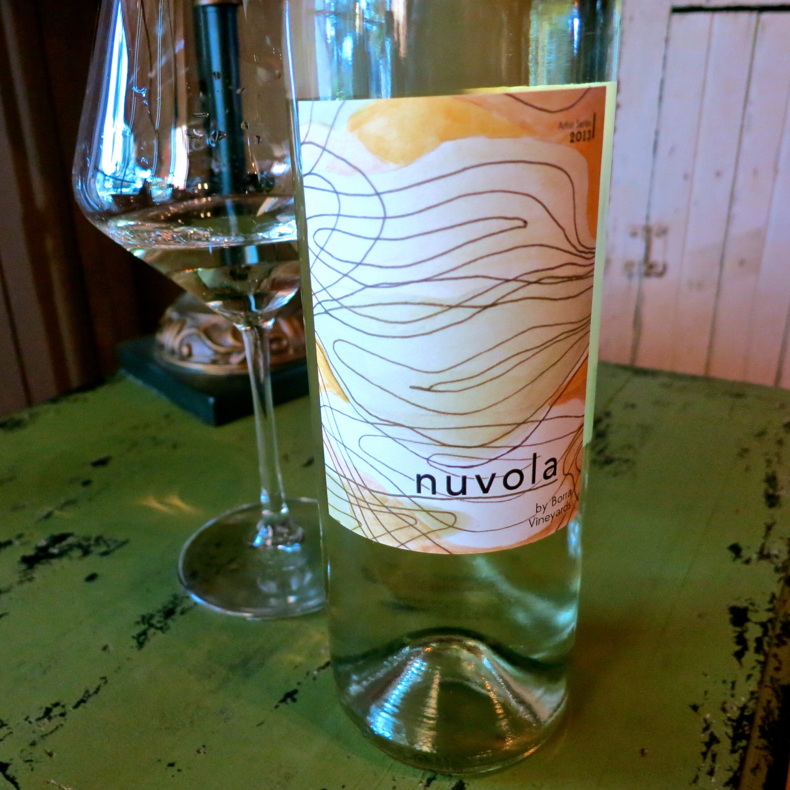 Nuvola white wine bottle with label featuring abstract lines, on a green table with a wine glass nearby.