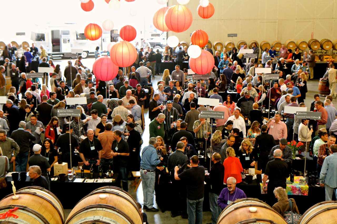 Crowd at Lodi Winegrape Commission event with wine barrels and booths.