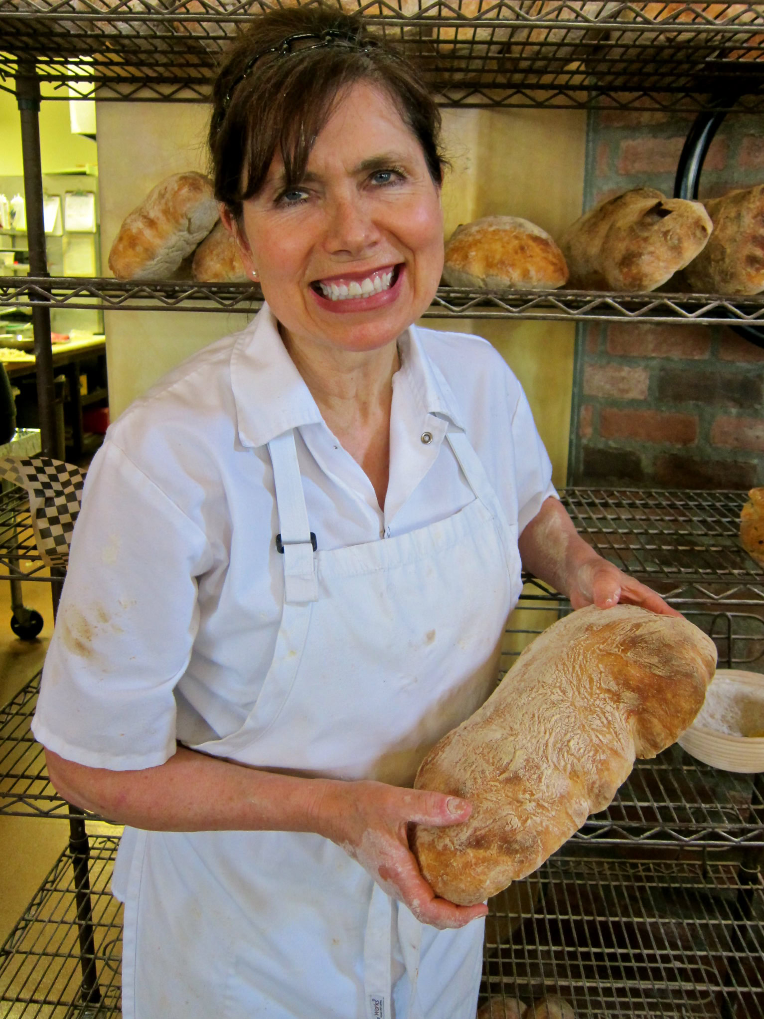 Woman baker holding a freshly baked loaf of bread in a bakery kitchen.