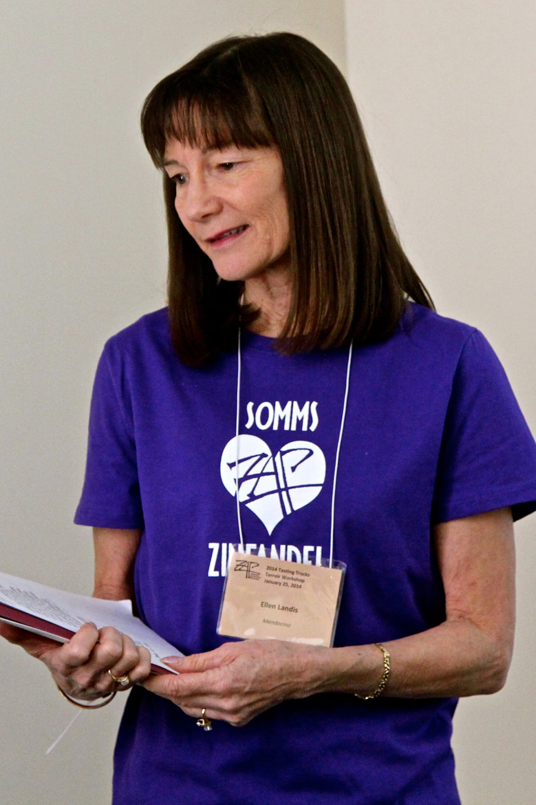 Woman wearing a blue T-shirt with Lodi Winegrape Commission logo, reading a booklet at an event.