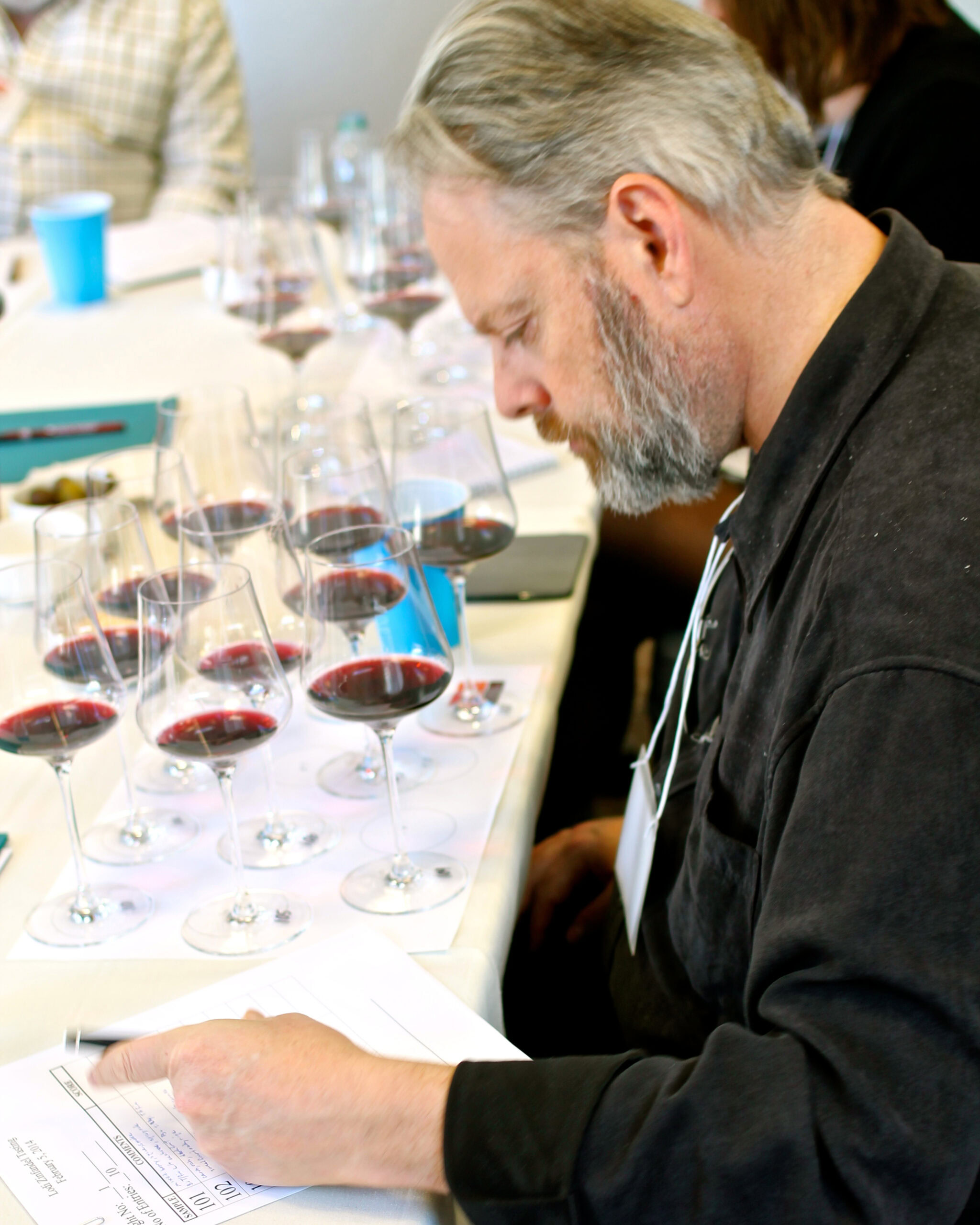 Man tasting red wine at a wine tasting event with multiple glasses of wine on the table.