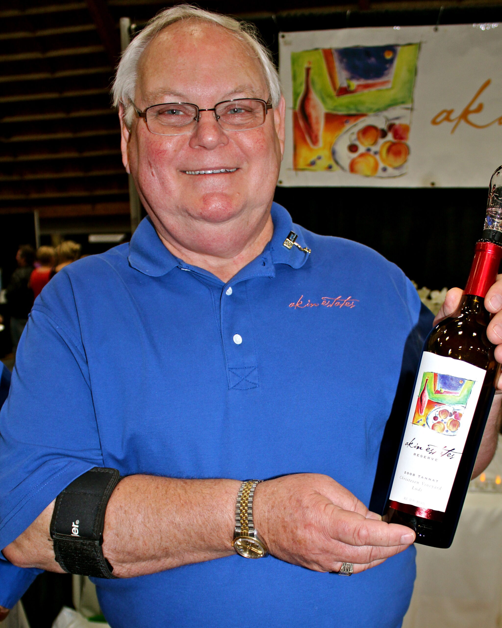 Smiling man in blue polo holding a wine bottle at a Lodi wine event.