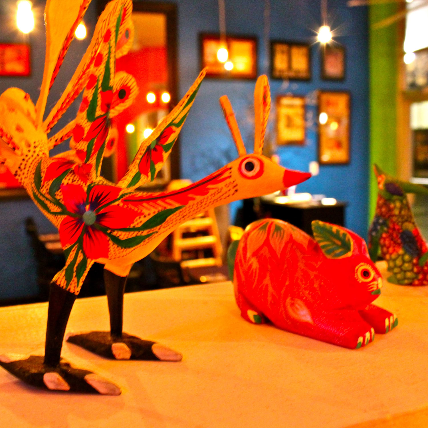 Vibrant Mexican folk art decorations including a bird and a rabbit on a table in a lively setting.