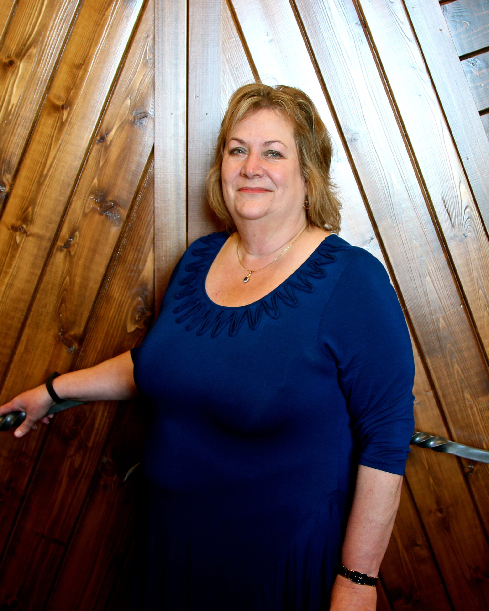 Woman in blue dress at Lodi Winegrape Commission event, wooden background, smiling.