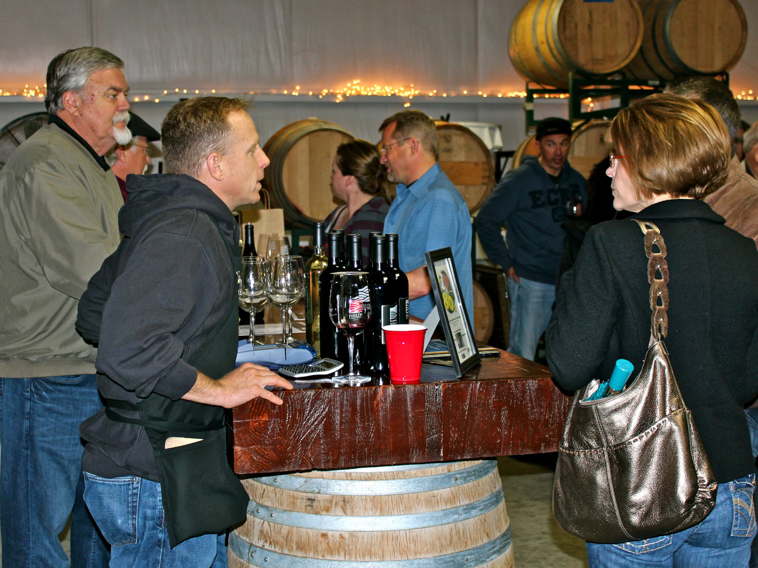 People tasting and discussing wine at a Lodi wine event with barrels in the background.