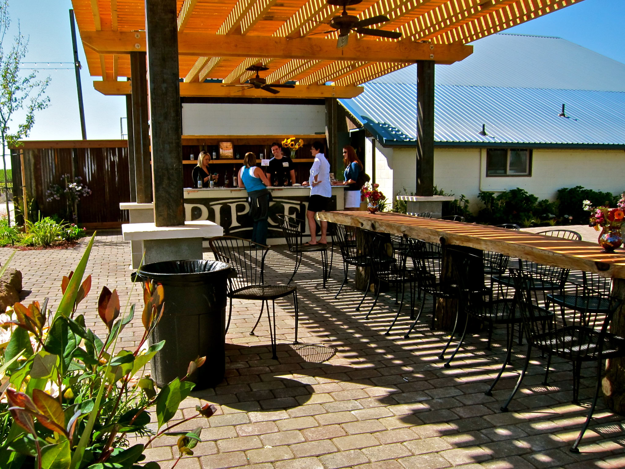 Outdoor patio at Lodi Winegrape Commission with seating, bar, and people enjoying drinks in sunny weather.