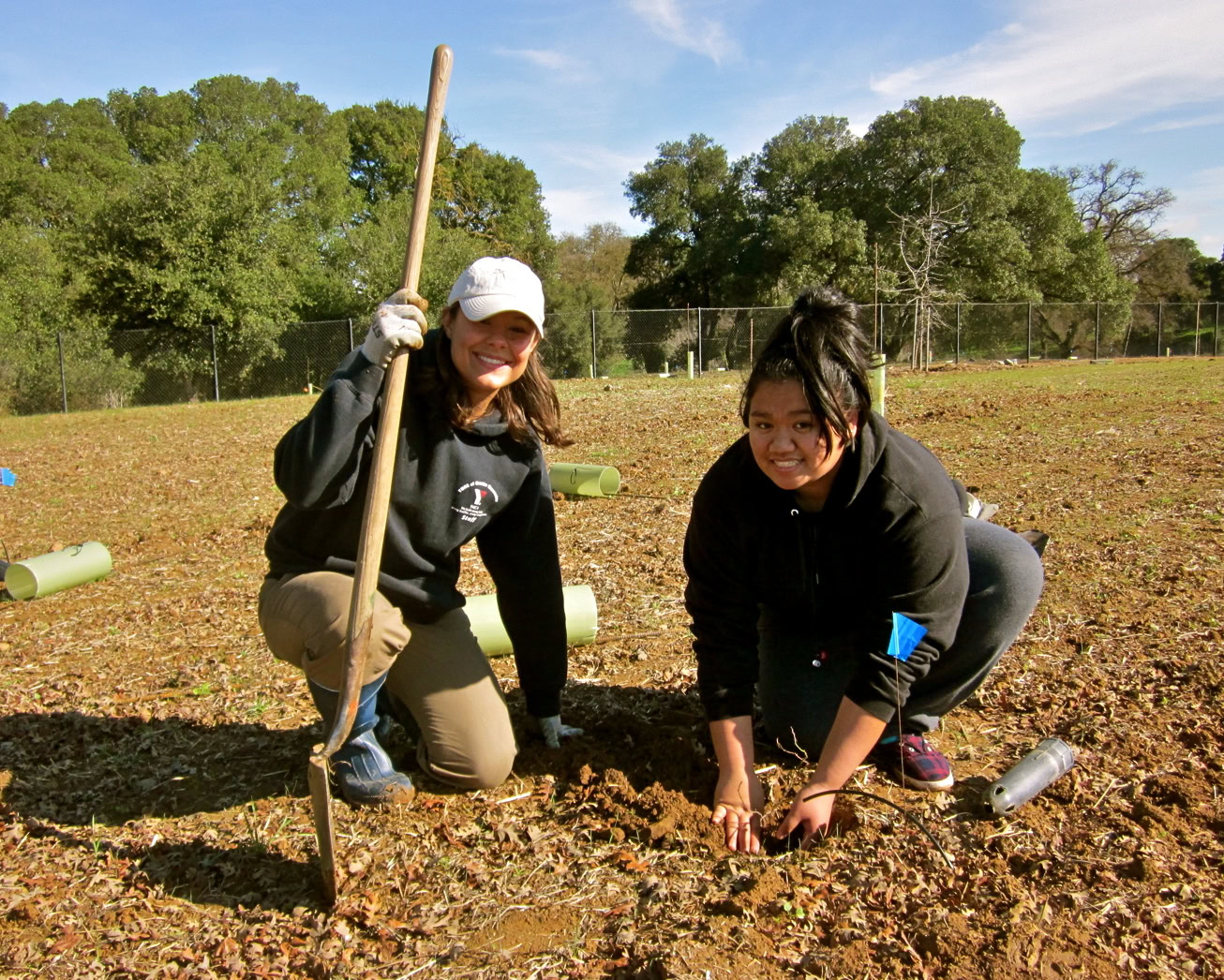 Two women planting grapevines in a vineyard during the Lodi Winegrape Commission event.