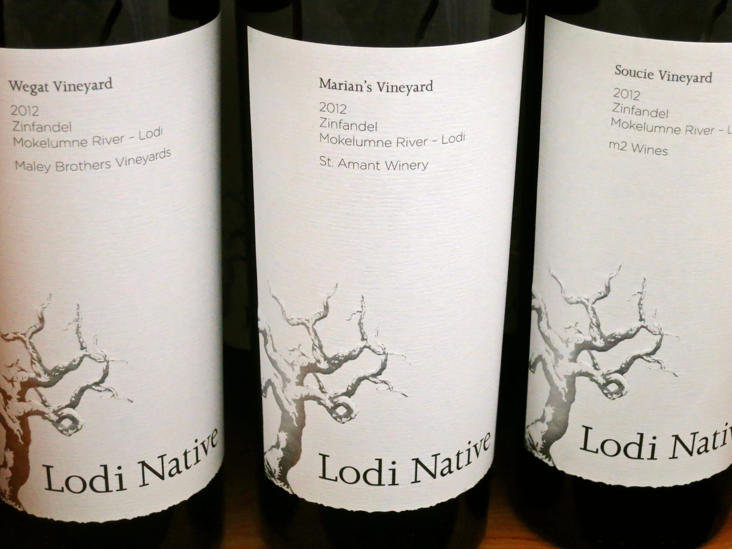 Three wine bottles from Lodi Native series showcasing Zinfandel wines from Mokelumne River vineyards.
