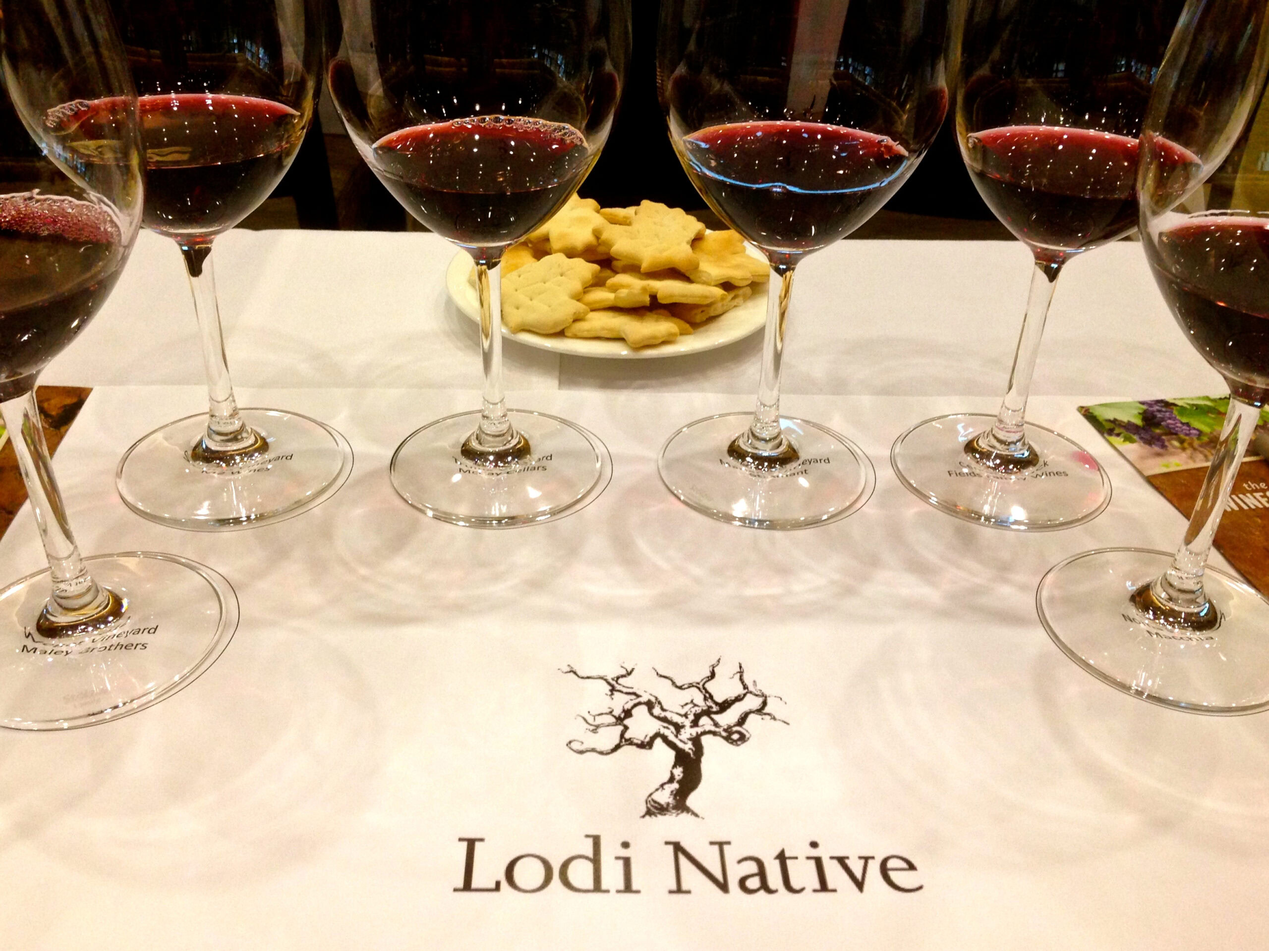 Five glasses of red wine on a table with a plate of cookies, representing Lodi Native wine tasting event.