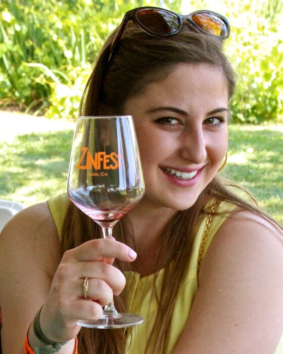 Smiling woman holding a wine glass with Lodi Winegrape Commission logo outdoors.