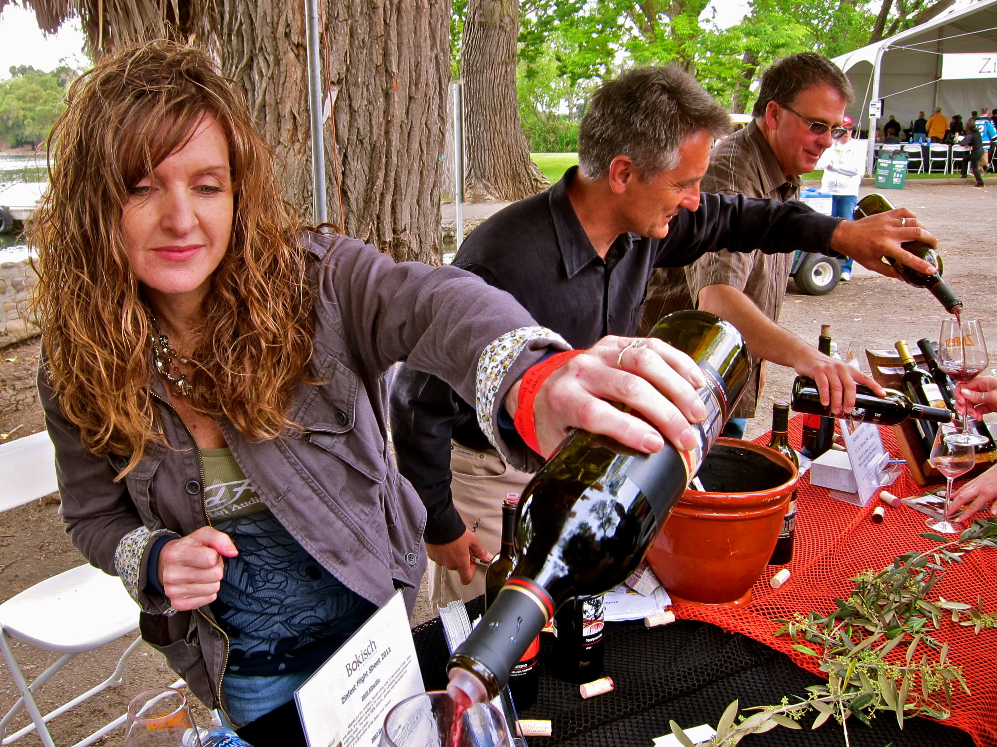People pouring wine at a Lodi Winegrape Commission event outdoors with trees in the background.