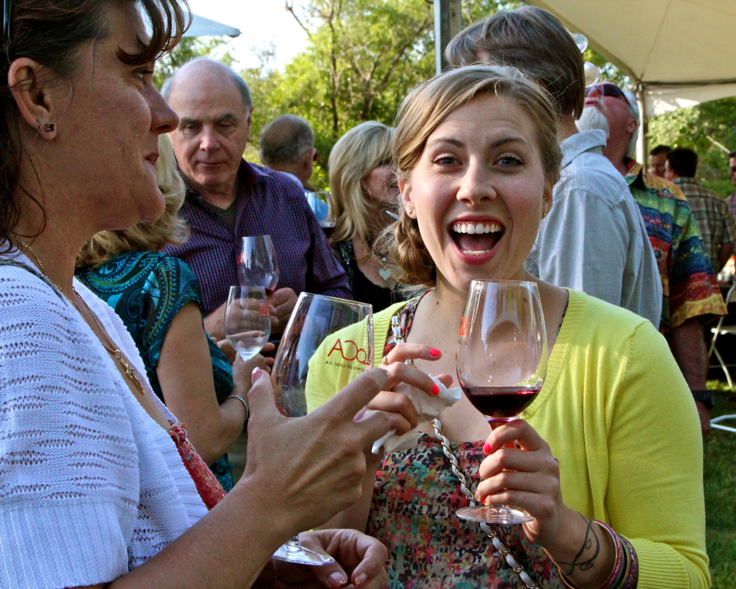 Young woman enjoying wine at Lodi Winegrape Commission outdoor event with friends.