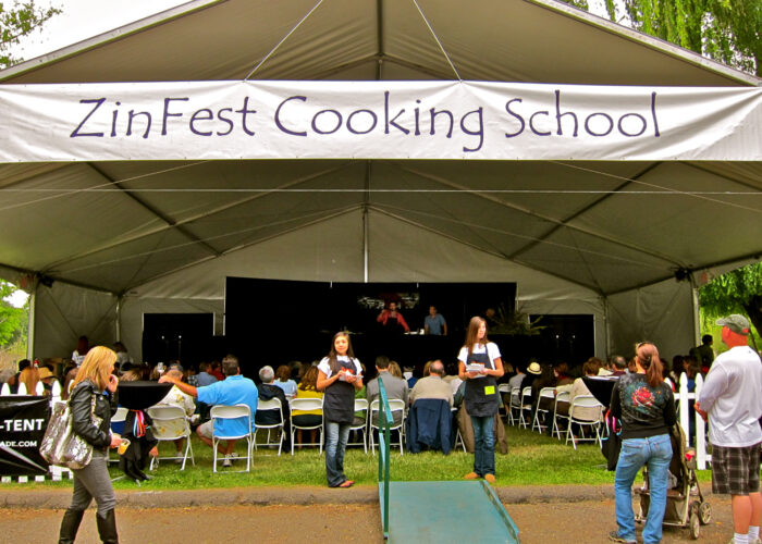 Crowd attending ZinFest Cooking School under a large white tent with a stage and cooking demonstrations.