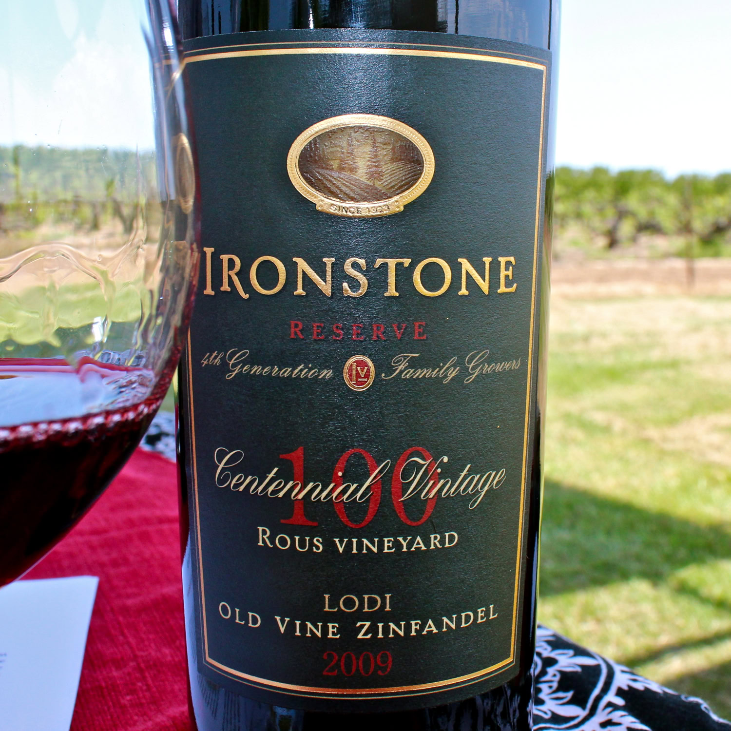 Bottle of Ironstone Reserve Centennial Vintage 2009 wine with glass of red wine outdoors.