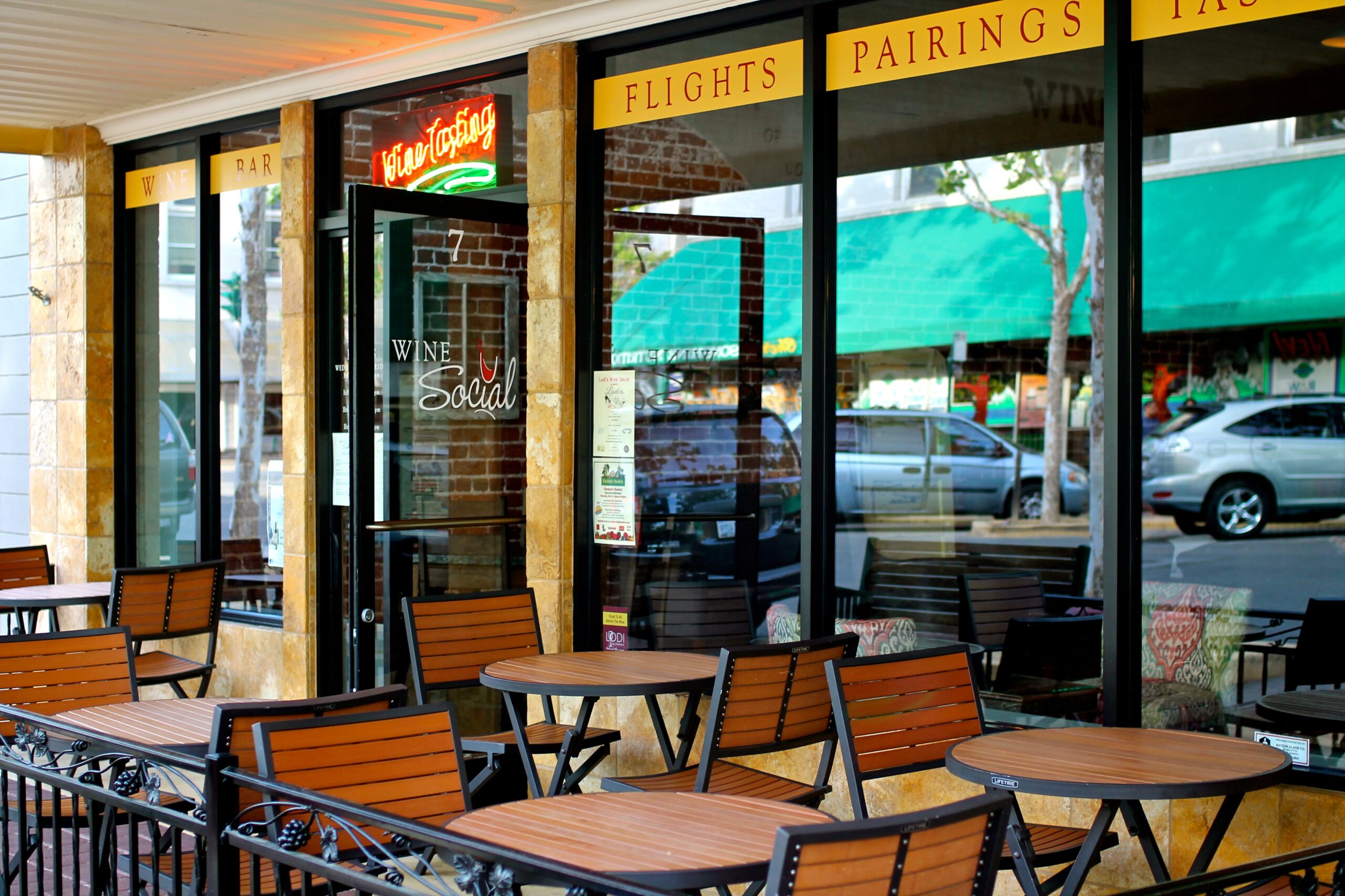 Outdoor seating area of a wine shop with tables and chairs, large glass windows, and signs for flights, pairings, and wine.