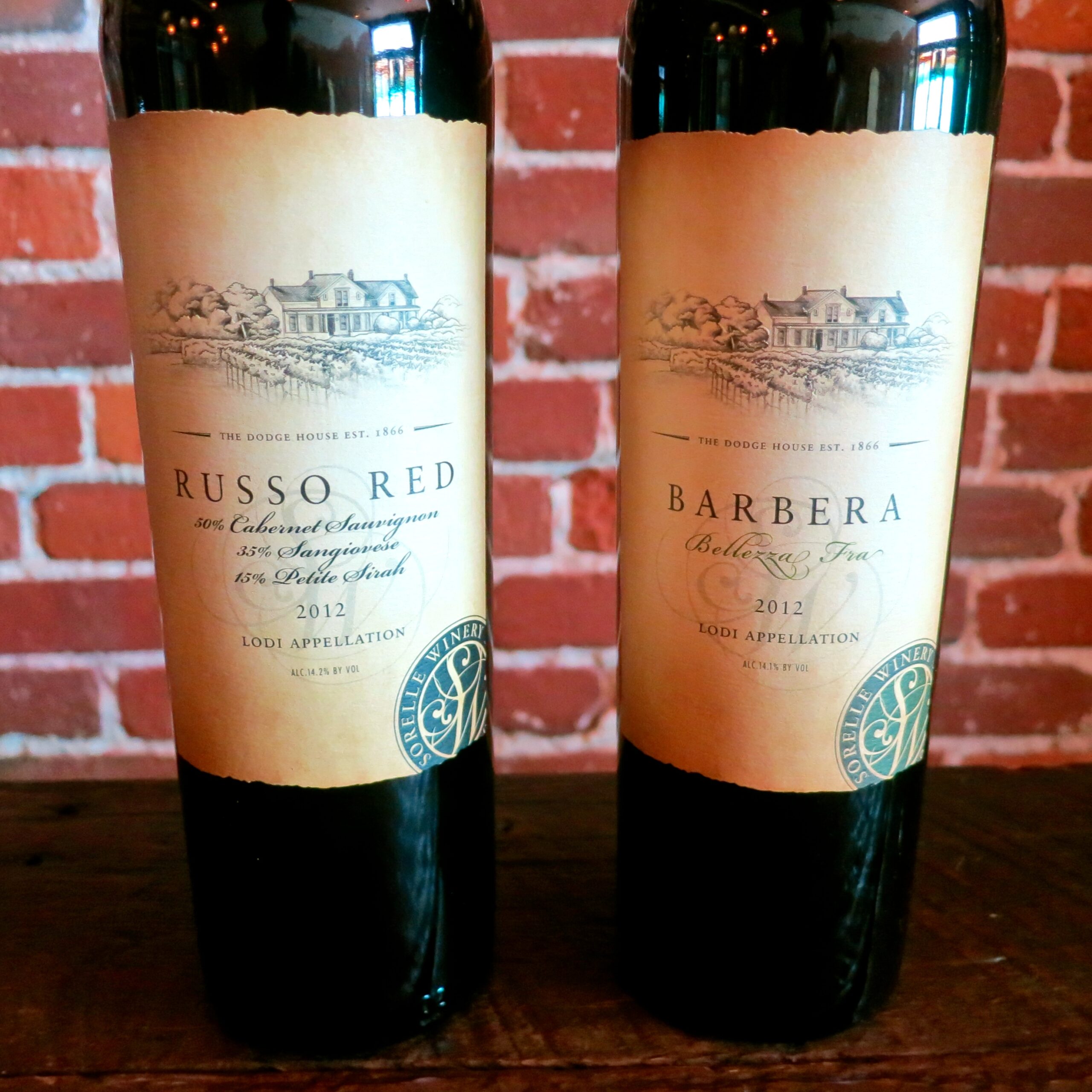 Two bottles of Lodi wine from the Lodi Winegrape Commission, featuring Russo Red and Barbera labels, on a wooden surface.
