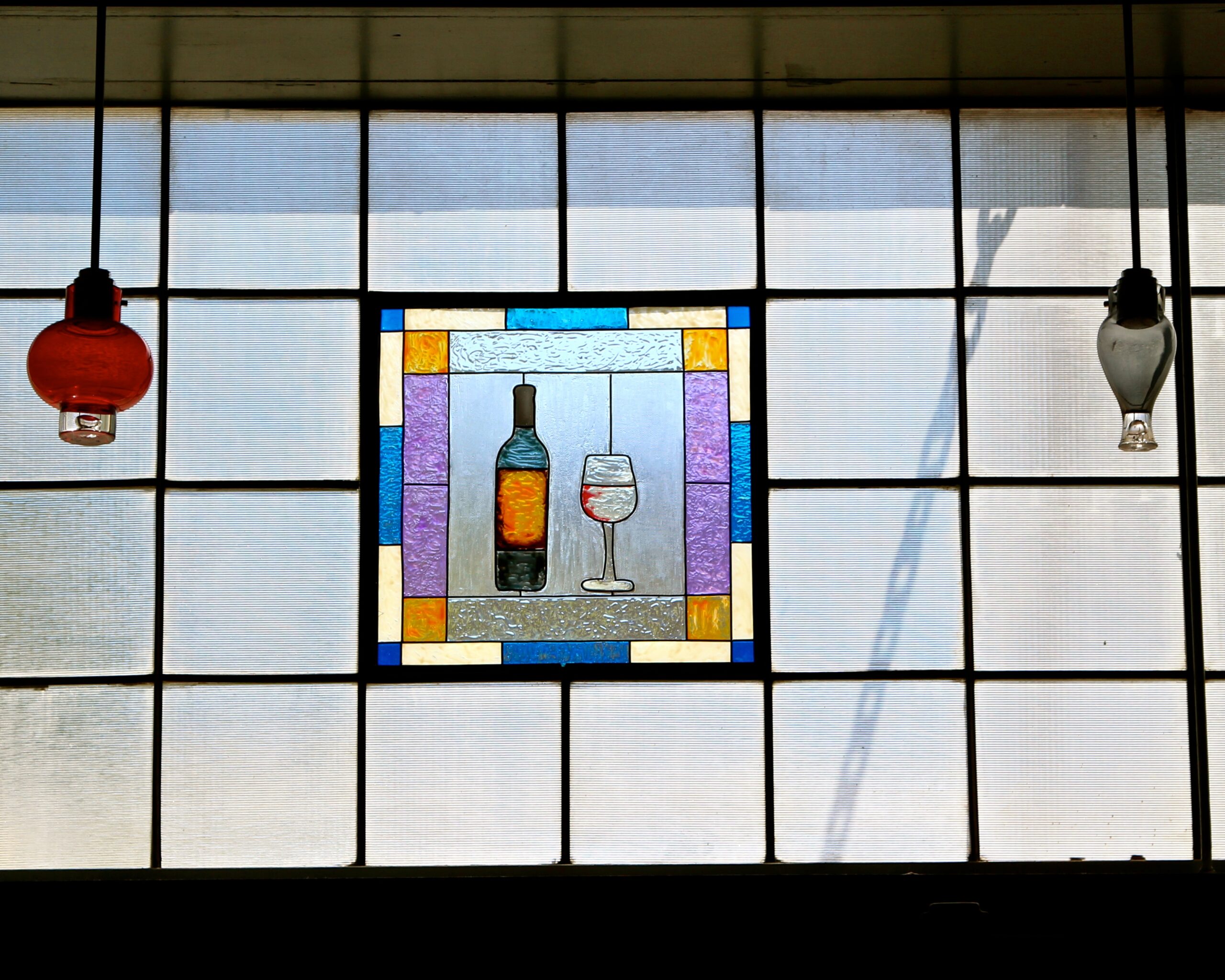 Stained glass window featuring a wine bottle and glass, with colorful border, in a modern industrial setting.
