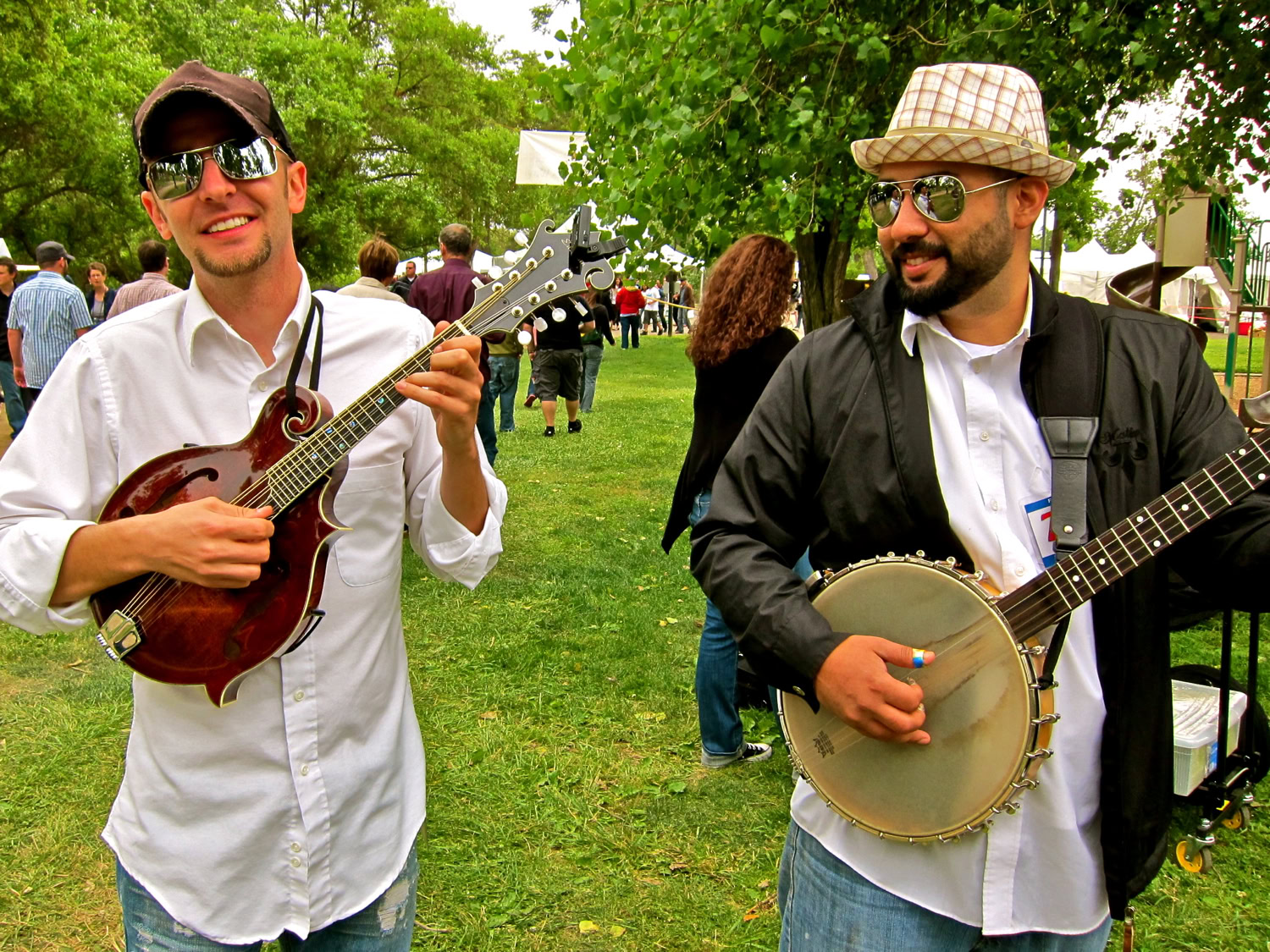 Two musicians playing string instruments at a Lodi wine event with trees and people in the background.
