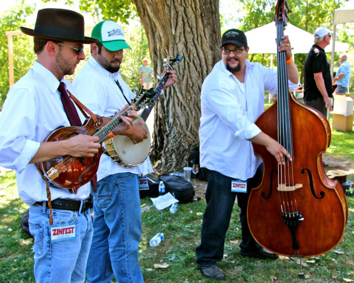 Musicians performing at Lodi Winegrape Commission event outdoors with trees and crowd in background.