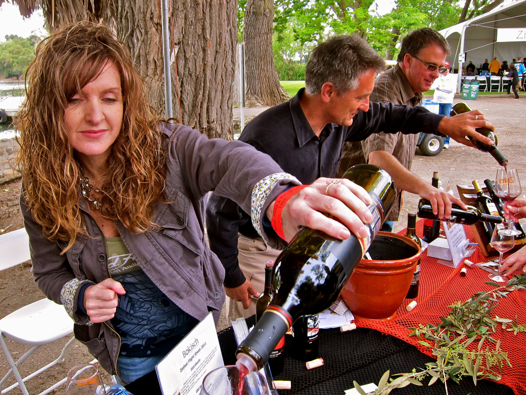 People tasting wine at a Lodi Winegrape Commission event outdoors with trees in the background.