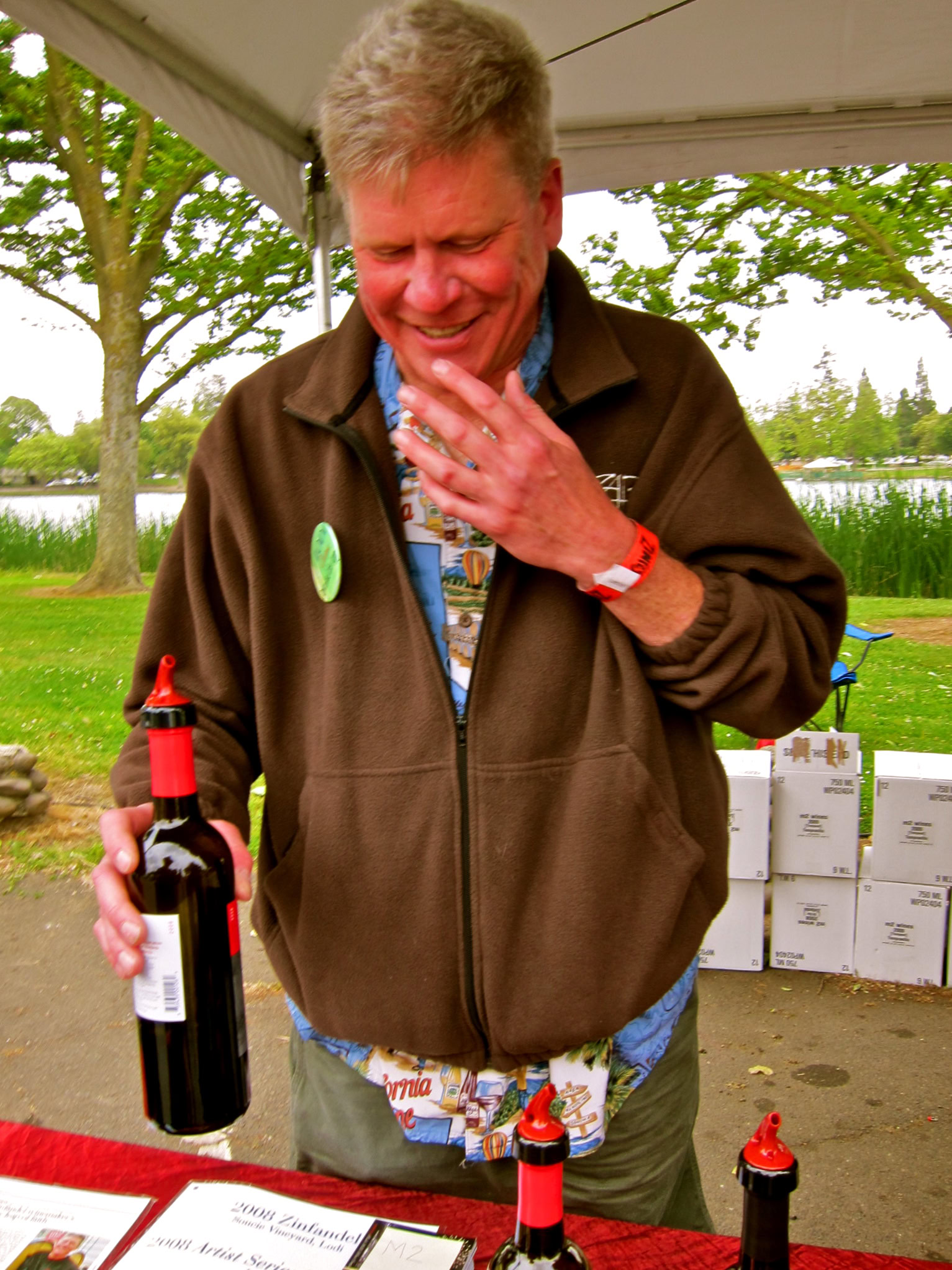 Man tasting wine at Lodi Winegrape Commission event outdoors with trees and lake in background.