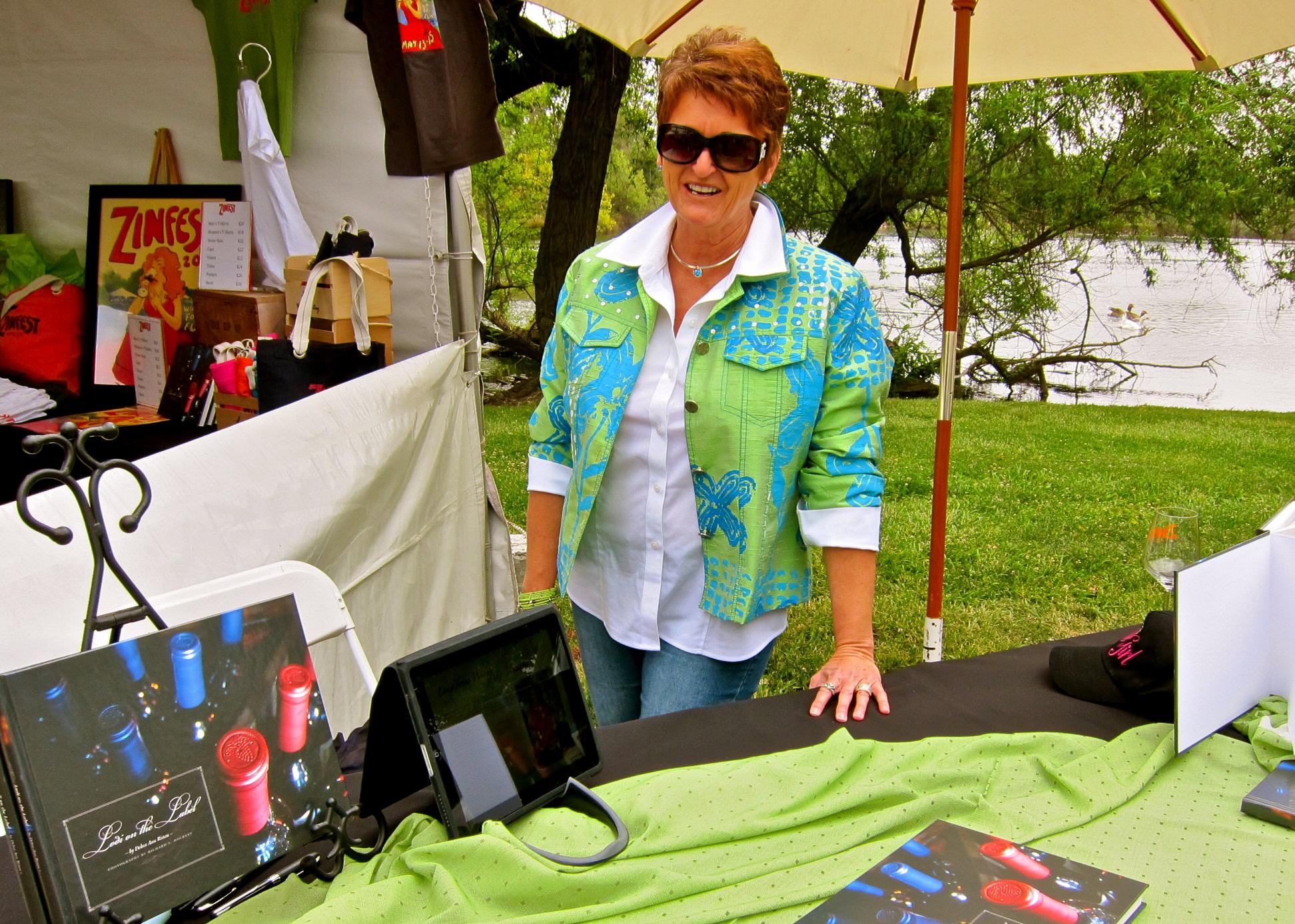 Woman at Lodi Winegrape Commission booth showcasing wine bottles and promotional materials outdoors.