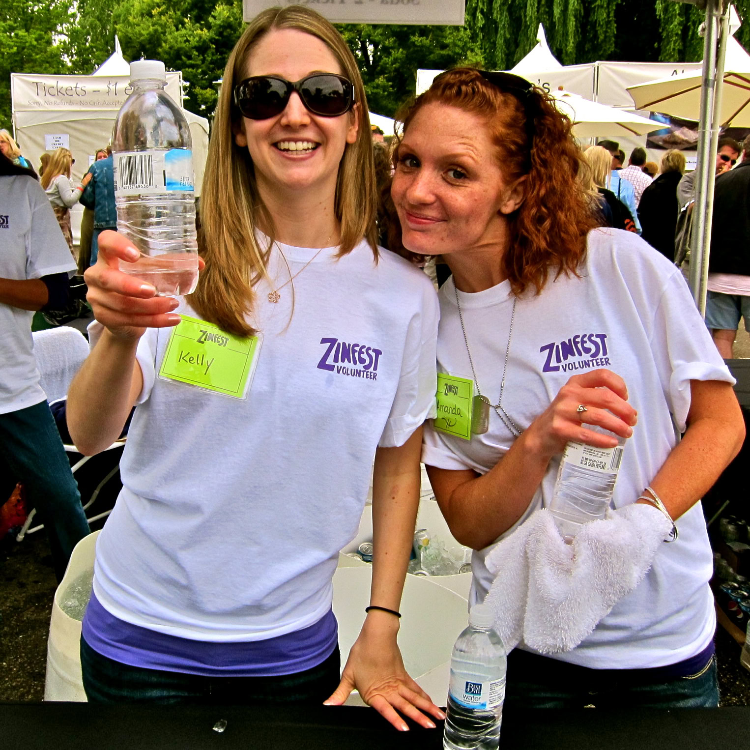 Two volunteers from Lodi Winegrape Commission smiling at an outdoor event, holding water bottles, wearing Zinfest volunteer T.