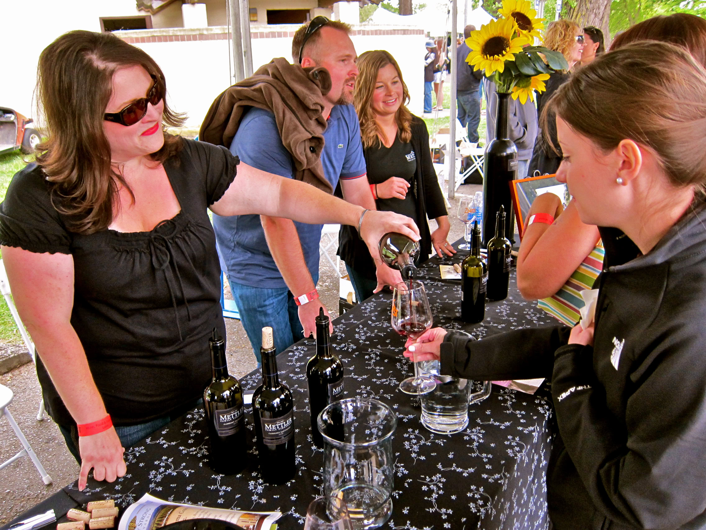 People enjoying wine tasting at Lodi Winegrape Commission event with bottles and glasses on table.