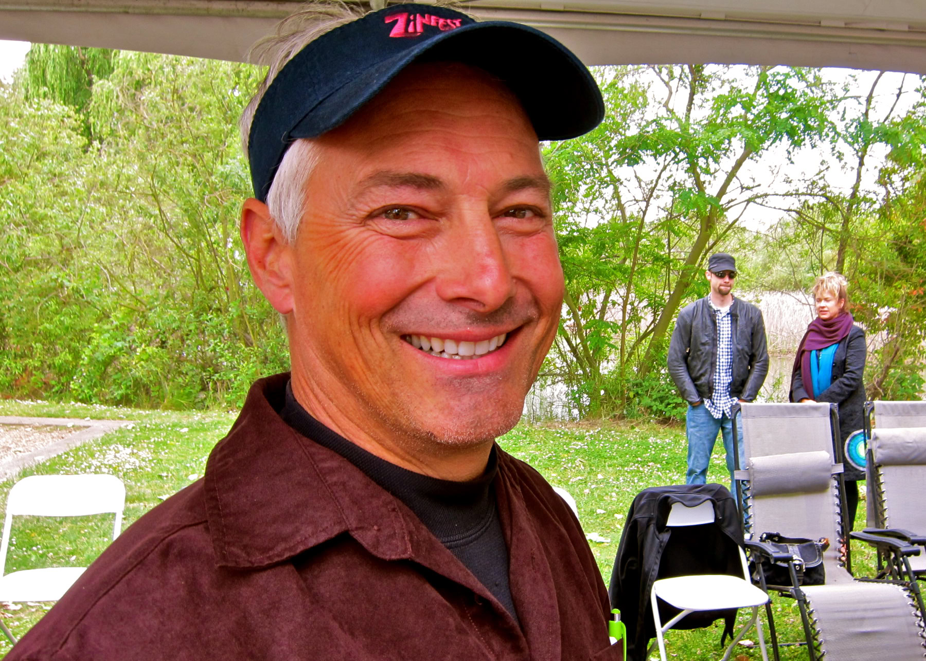 Smiling man at Lodi Winegrape Commission event outdoors with people and chairs in background.