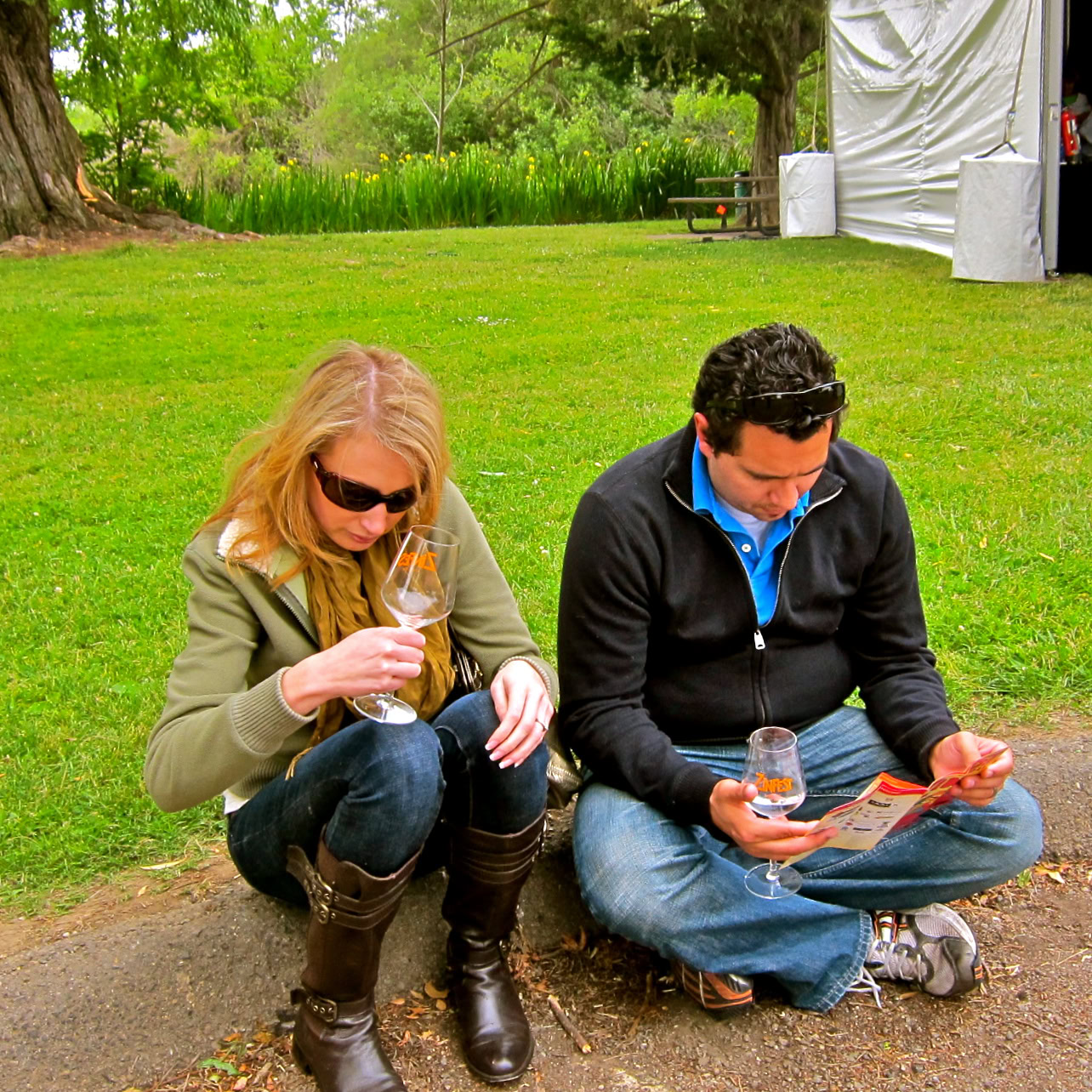 Two people enjoying wine outdoors at a Lodi wine event, sitting on grass with wine glasses in hand.