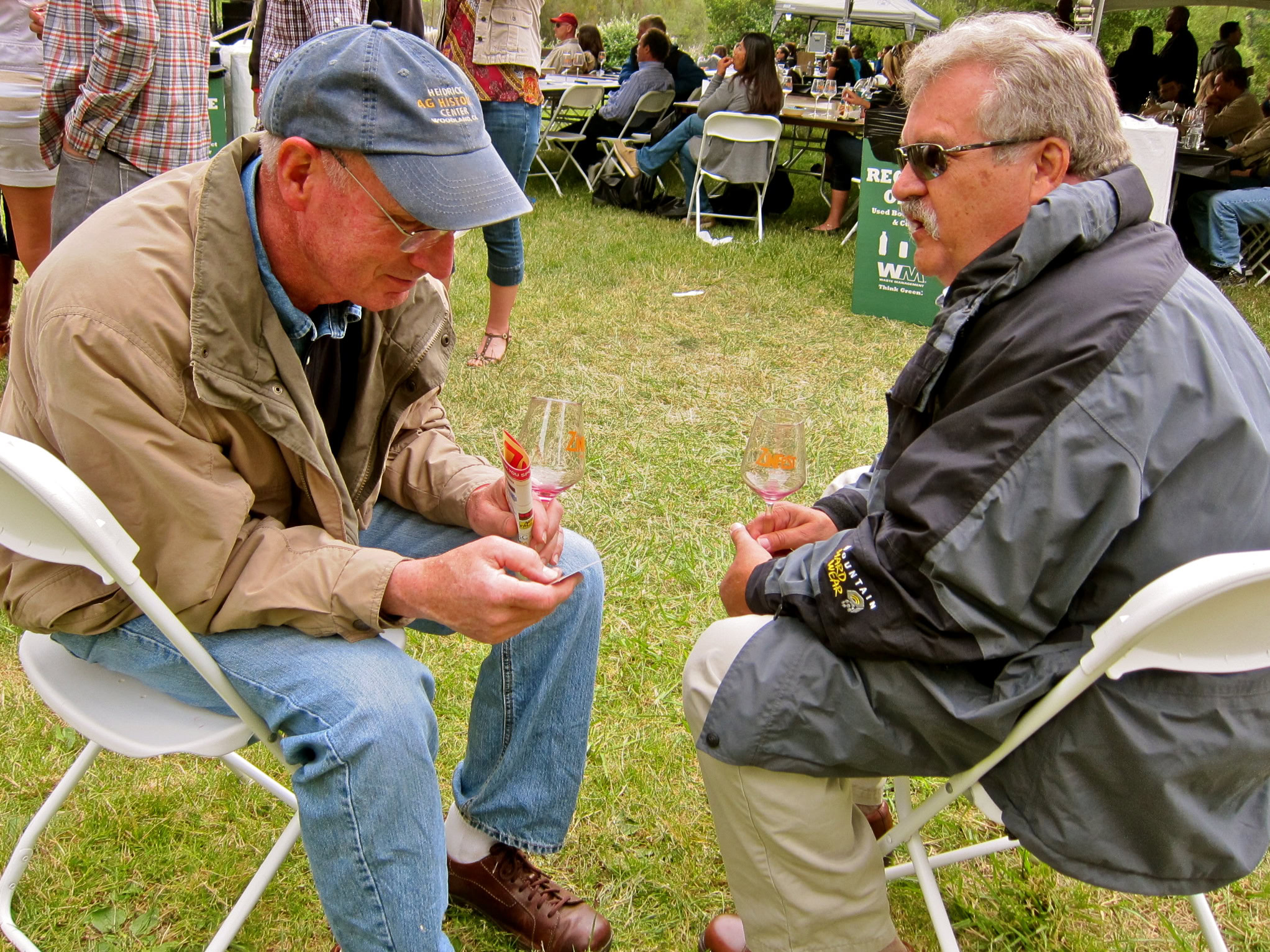 Two men tasting wine outdoors at a Lodi Winegrape Commission event, with other attendees in the background.