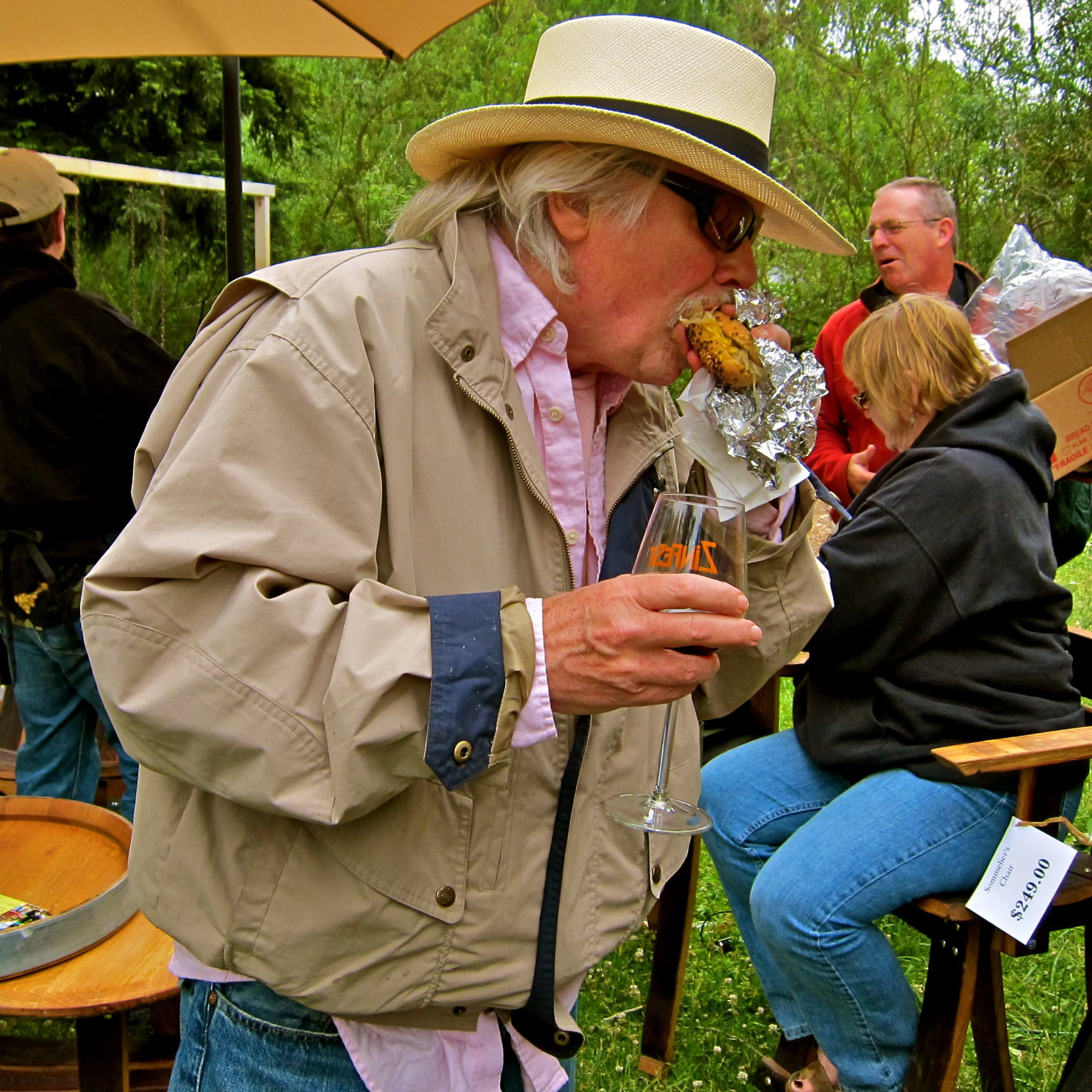 Elderly man enjoying wine and food at outdoor Lodi wine event with others in the background.