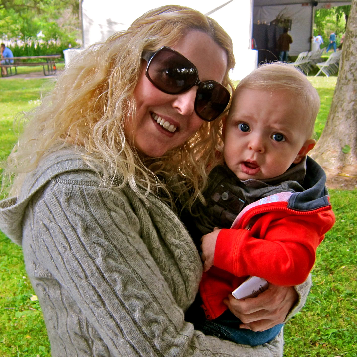 Woman with sunglasses holding a surprised baby at a Lodi wine event outdoors.
