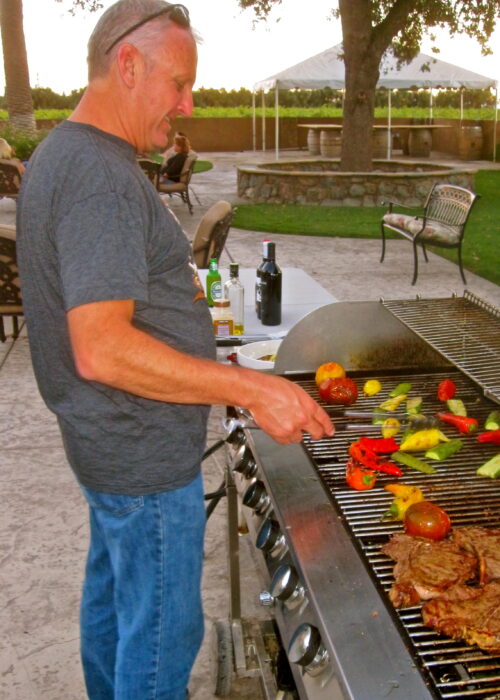 Man grilling vegetables and steaks outdoors at a Lodi wine region event.
