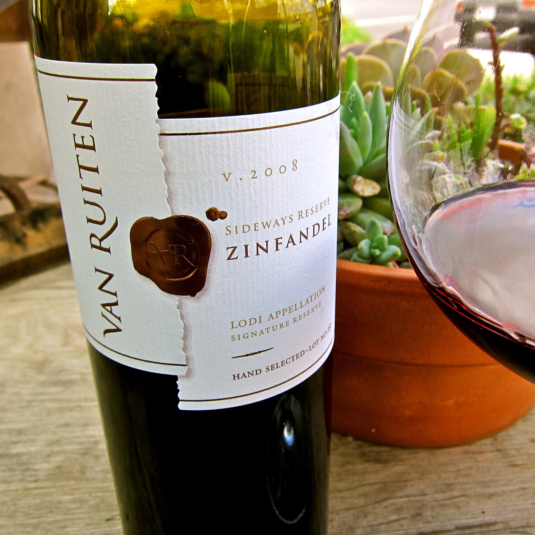 Lodi Zinfandel wine bottle from Van Ruiten with a glass of red wine and succulents in the background.
