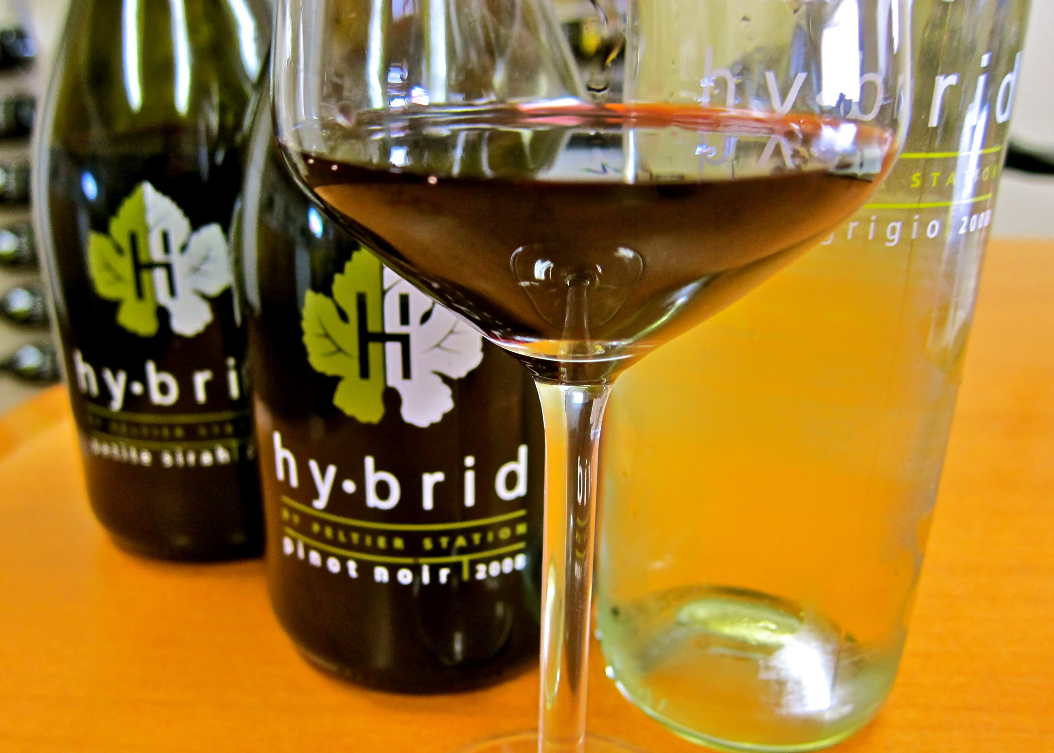 Close-up of a glass of red wine with hybrid wine bottles in the background, on a wooden surface.