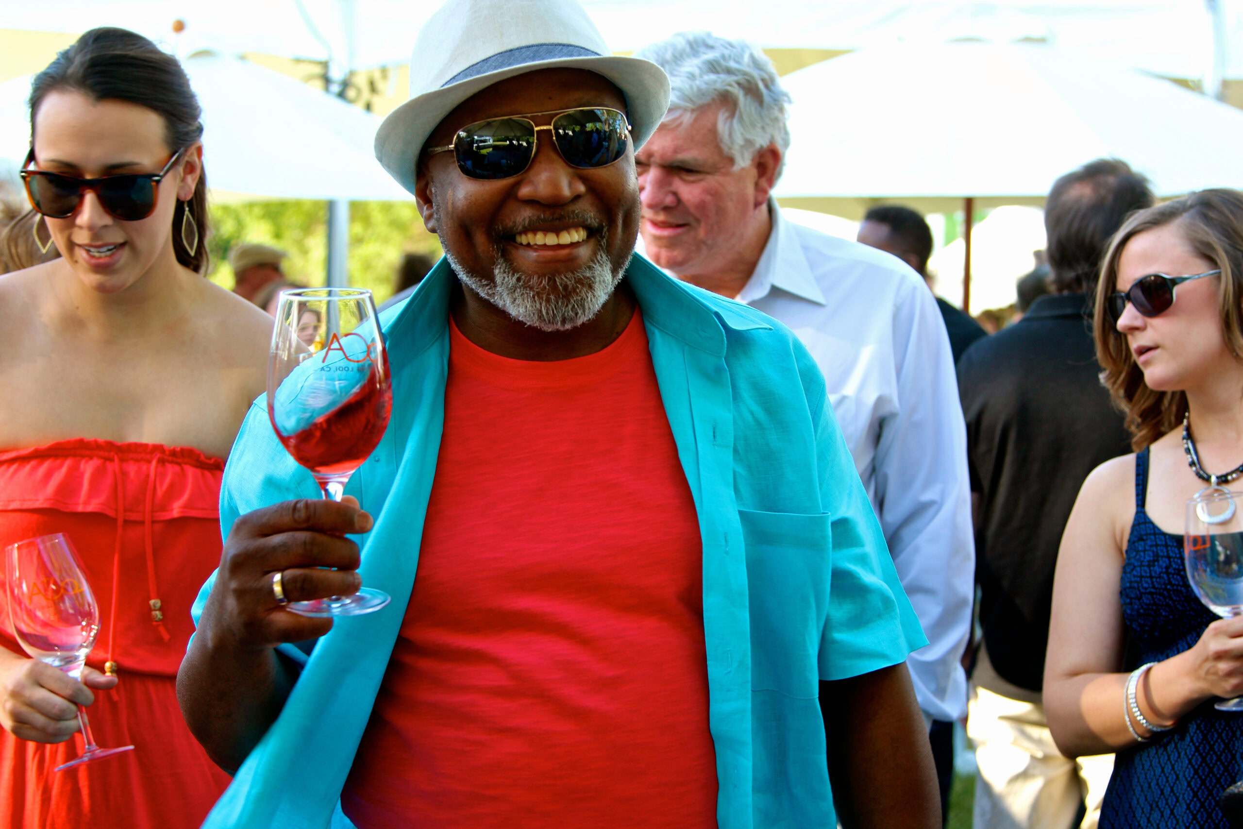 Smiling man with sunglasses holding a glass of rosé wine at a wine tasting event.