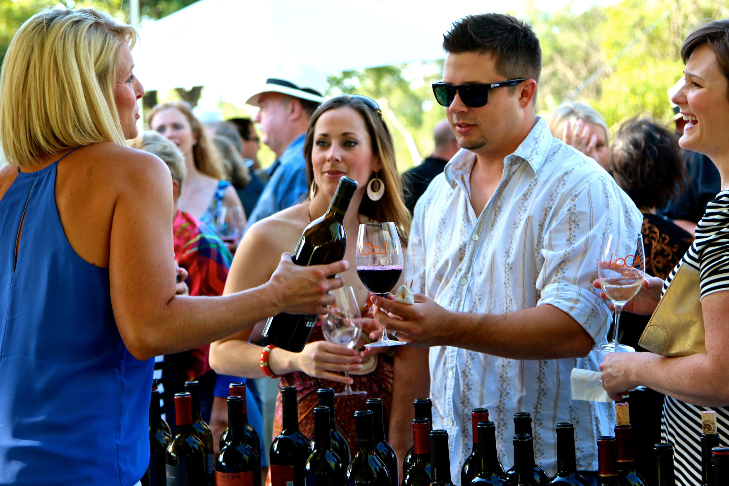People enjoying wine tasting at an outdoor event with bottles and glasses of wine.