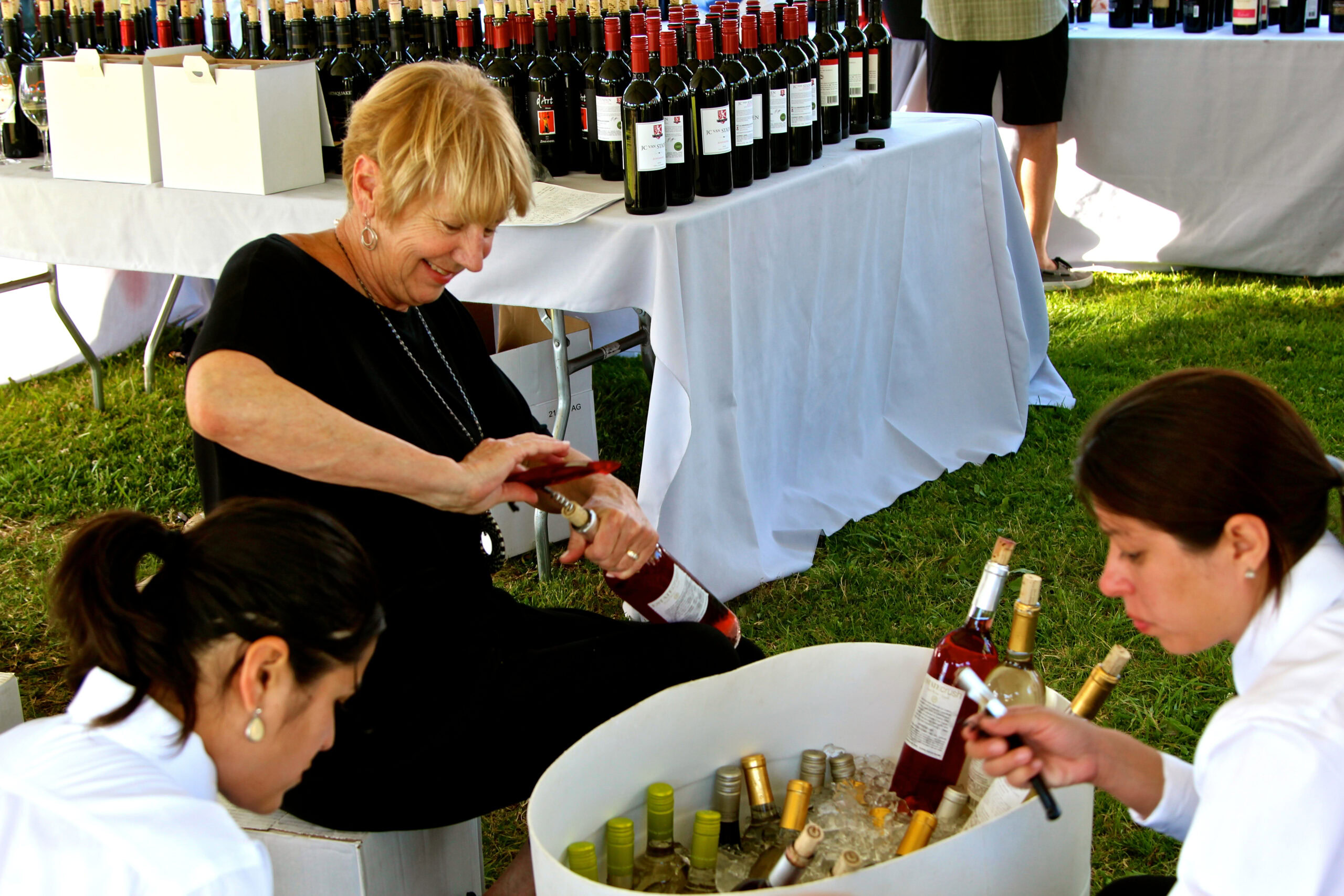 Women enjoying wine tasting at Lodi Winegrape Commission event with wine bottles on display.