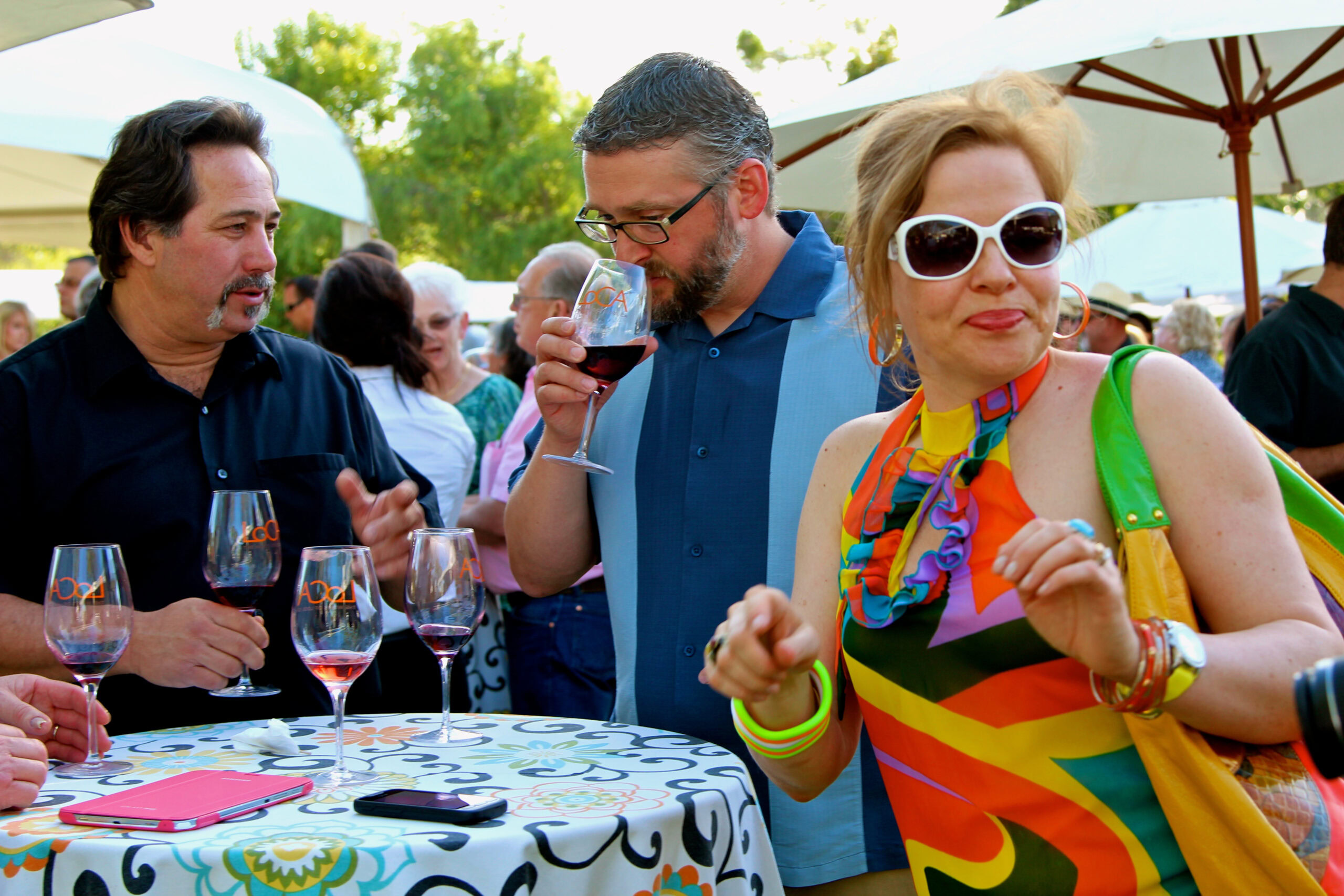 People enjoying wine tasting at an outdoor event with wine glasses and colorful attire.