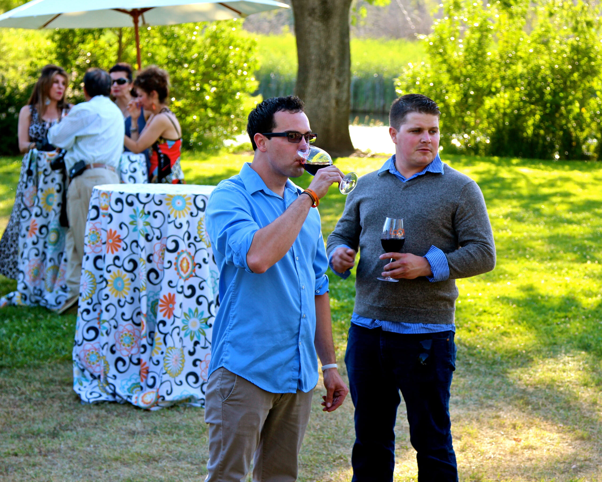 People enjoying wine tasting outdoors at a Lodi Winegrape Commission event with lush greenery and sunny weather.