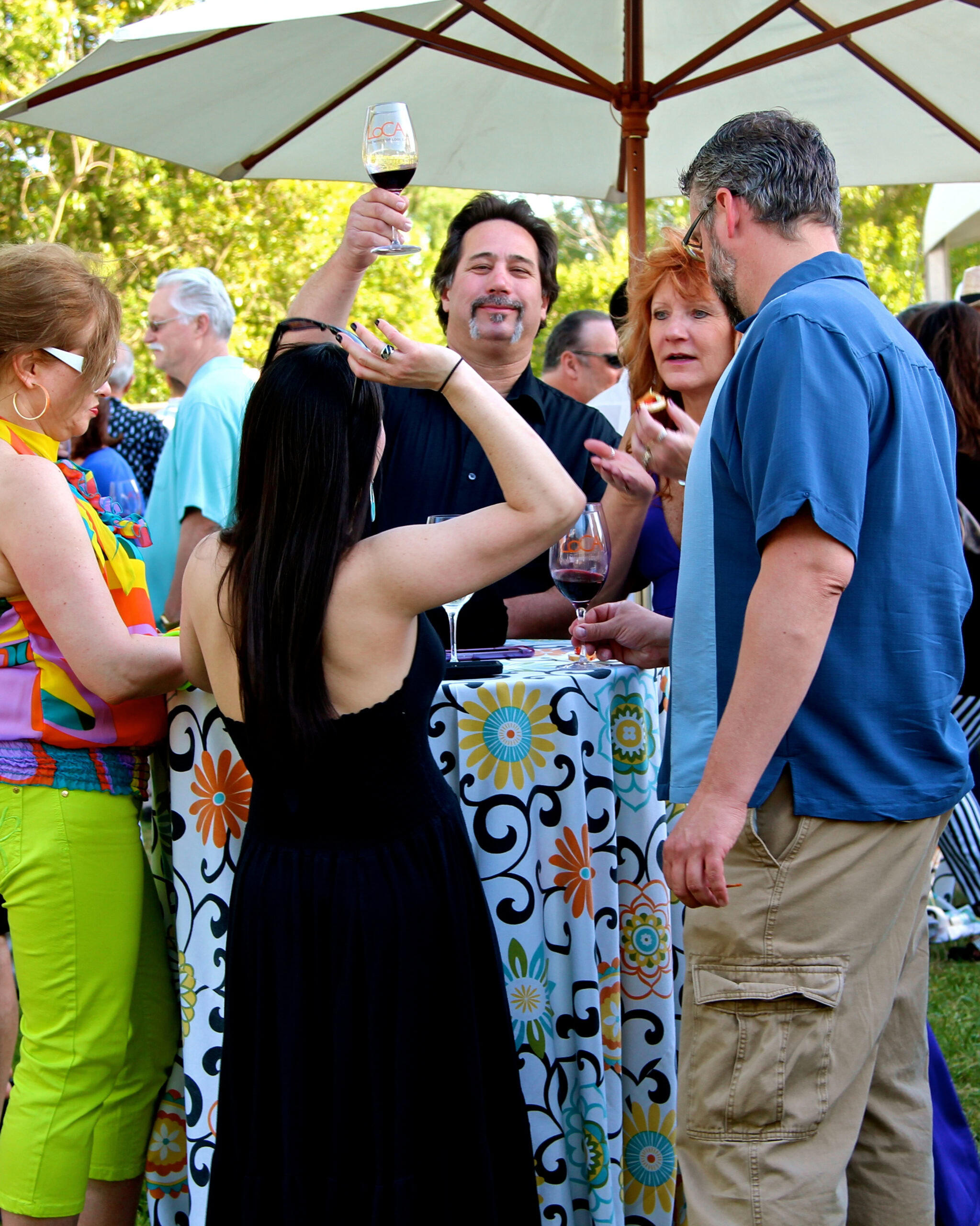 People enjoying wine tasting at an outdoor event with a table and umbrella, celebrating Lodi wine culture.