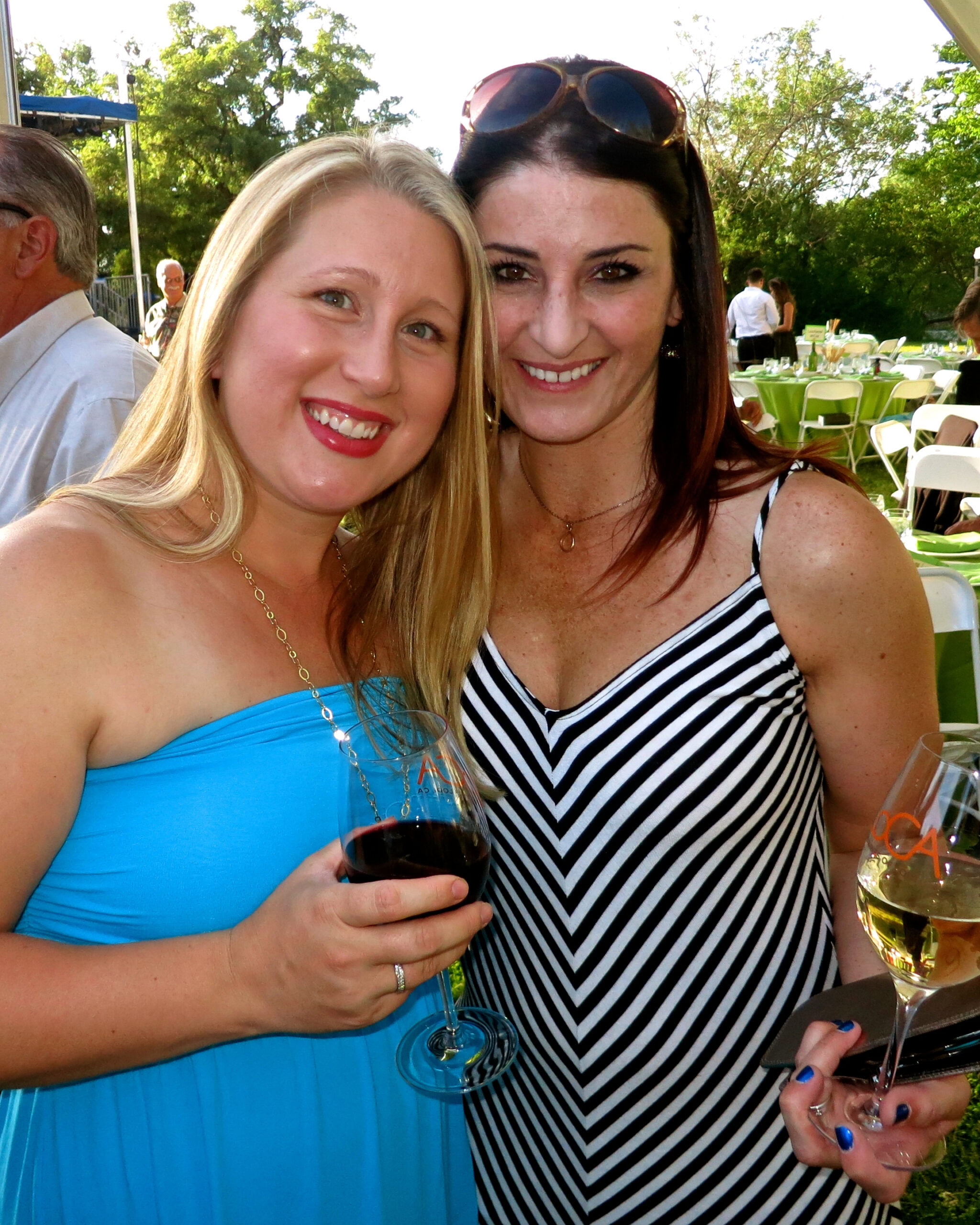 Two women enjoying wine at an outdoor event, smiling and holding glasses of red and white wine.